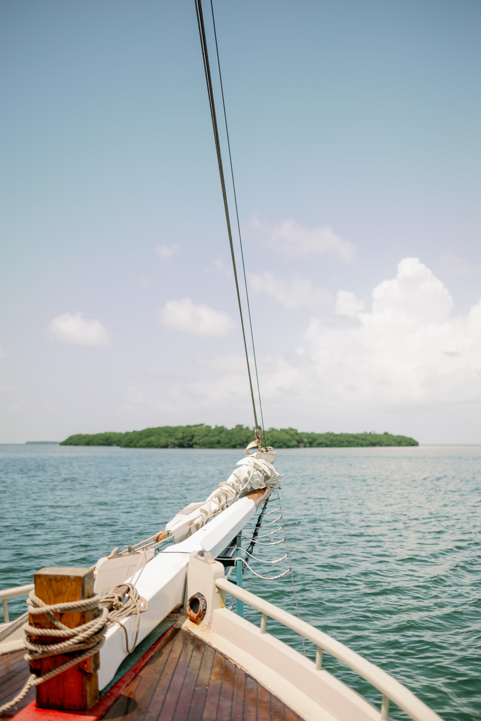 bow of a sailboat with wooden flooring, pointed toward a small mangrove island