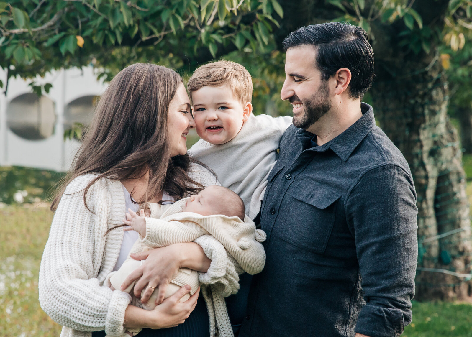 Lifestyle portrait of newborn baby and big brother embracing with mom and dad.