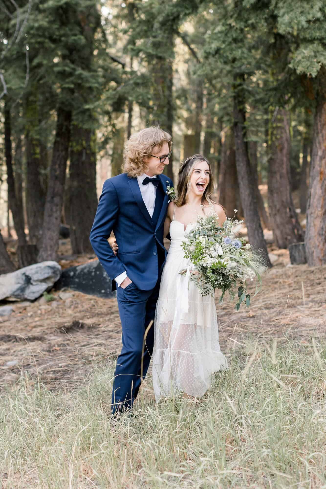 A bride and groom laugh together while standing in front of pine trees in Mammoth Lakes. 