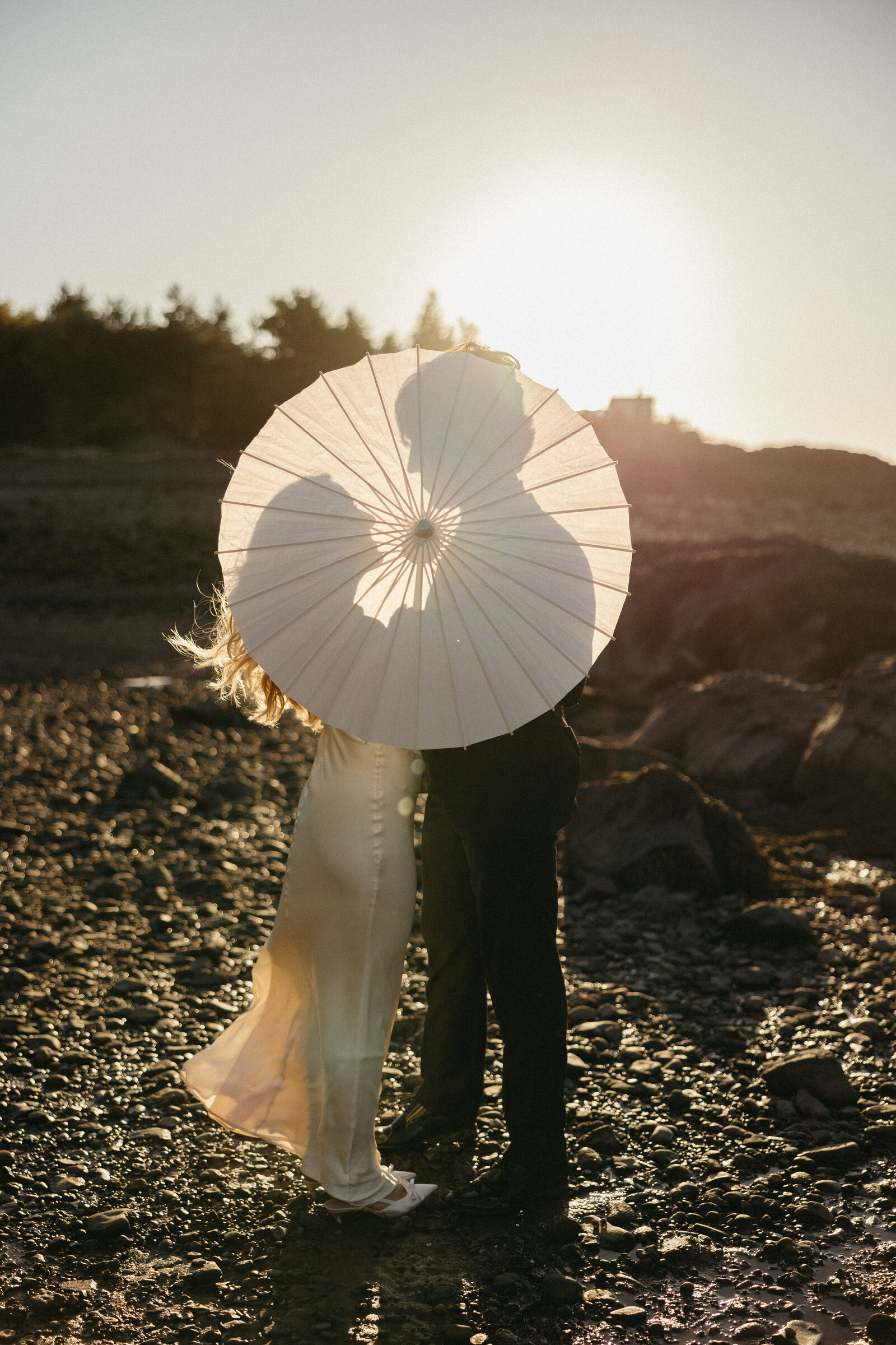 A bride and groom share a kiss behind a parasol at sunset in Nova Scotia. 