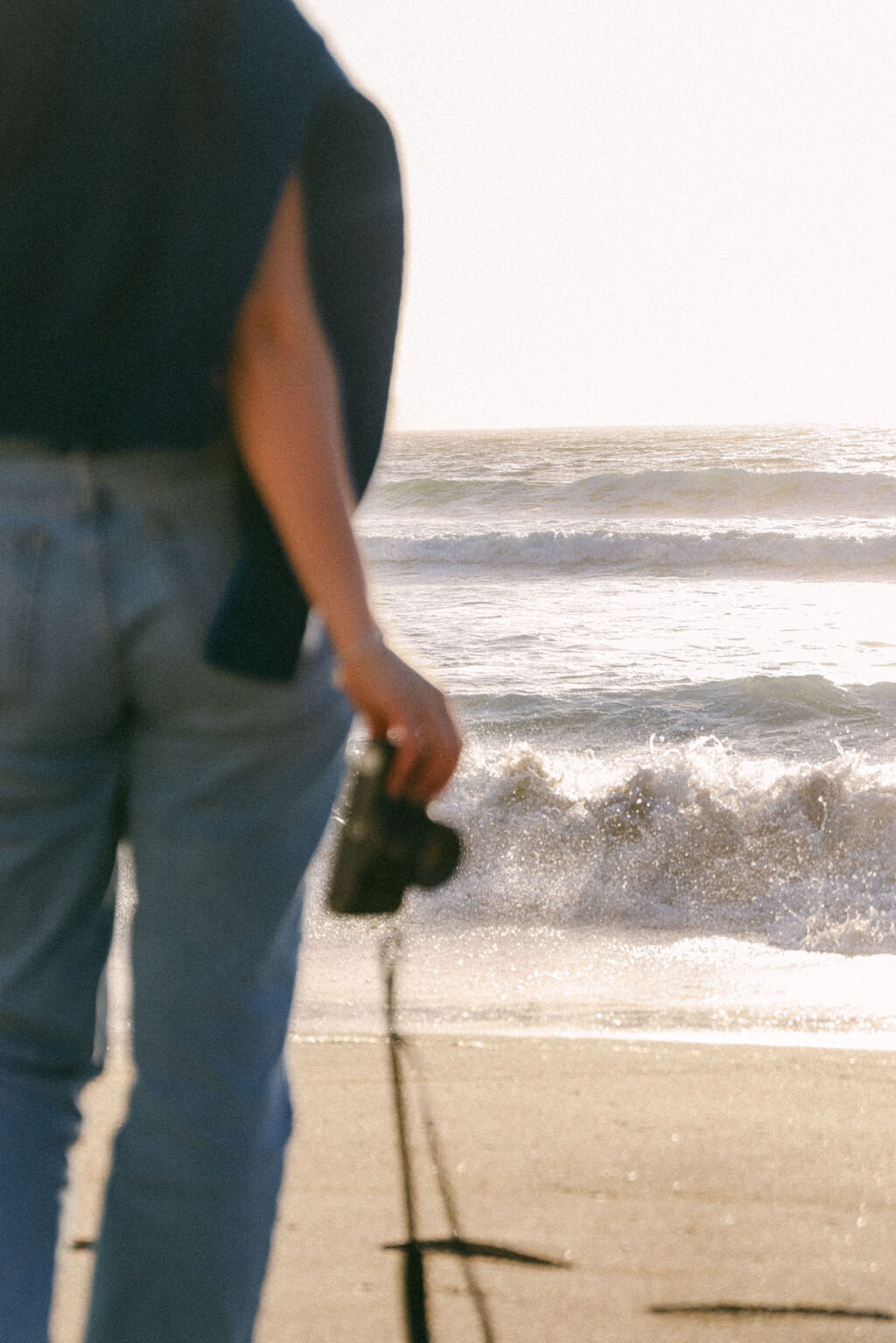 girl on beach with film camera looking at ocean