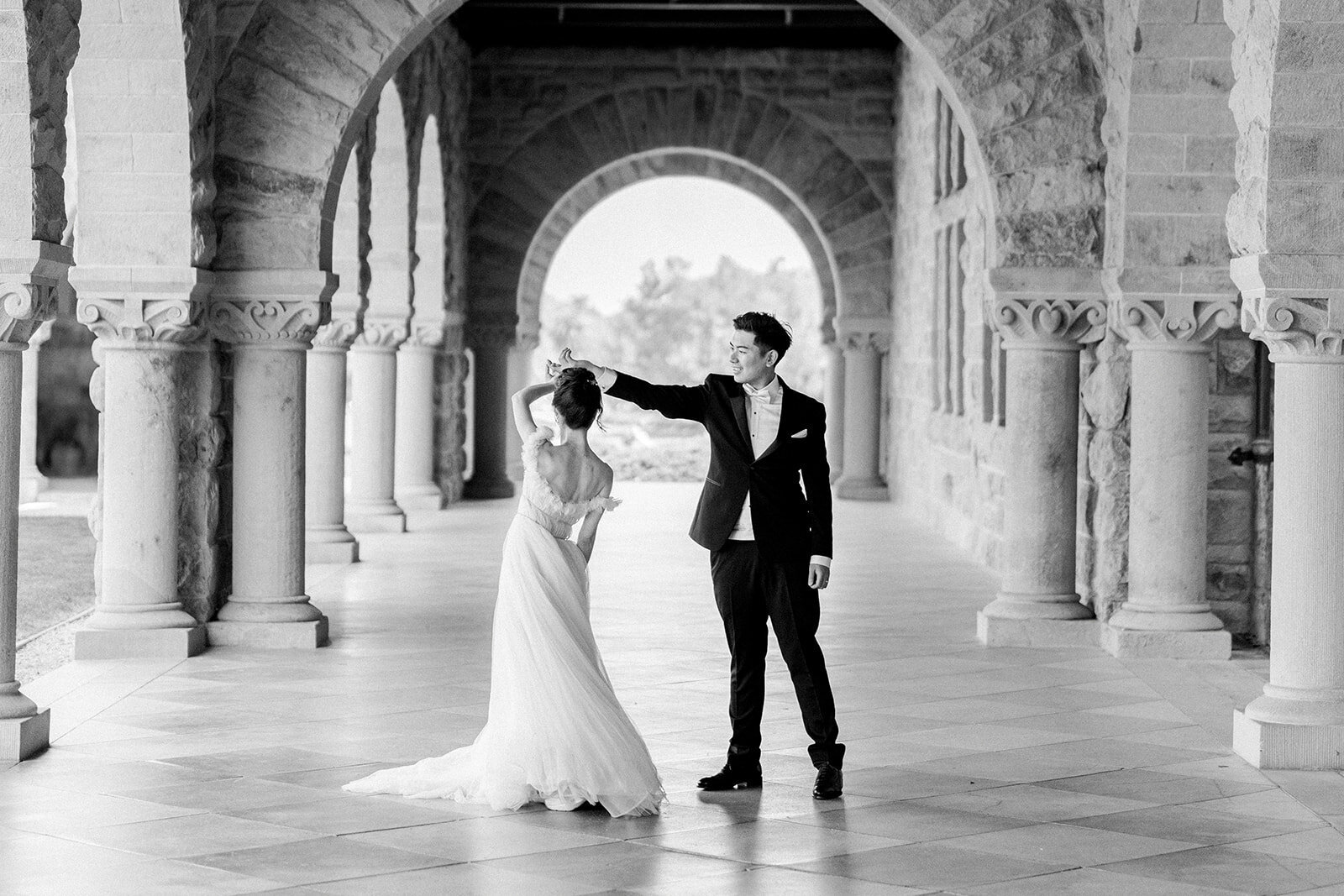 The bride and groom share a joyful dance under the arches of Stanford University, capturing a perfect wedding moment.