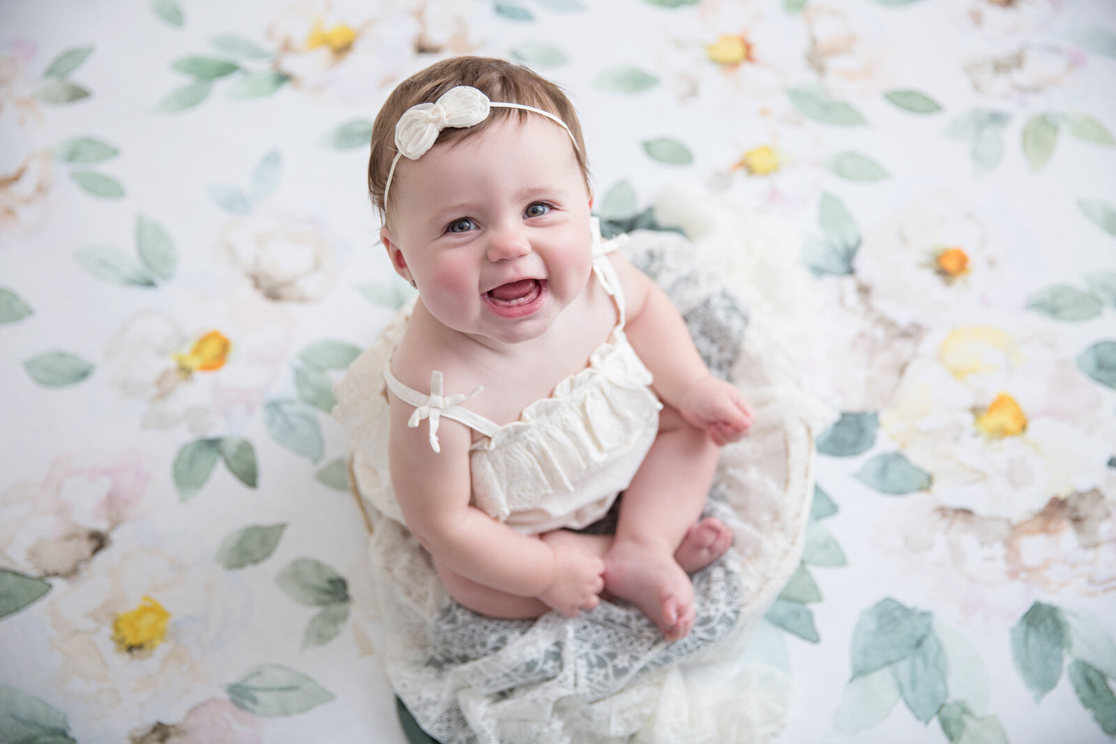 smiling baby girl in a wooden bowl with floral backdrop