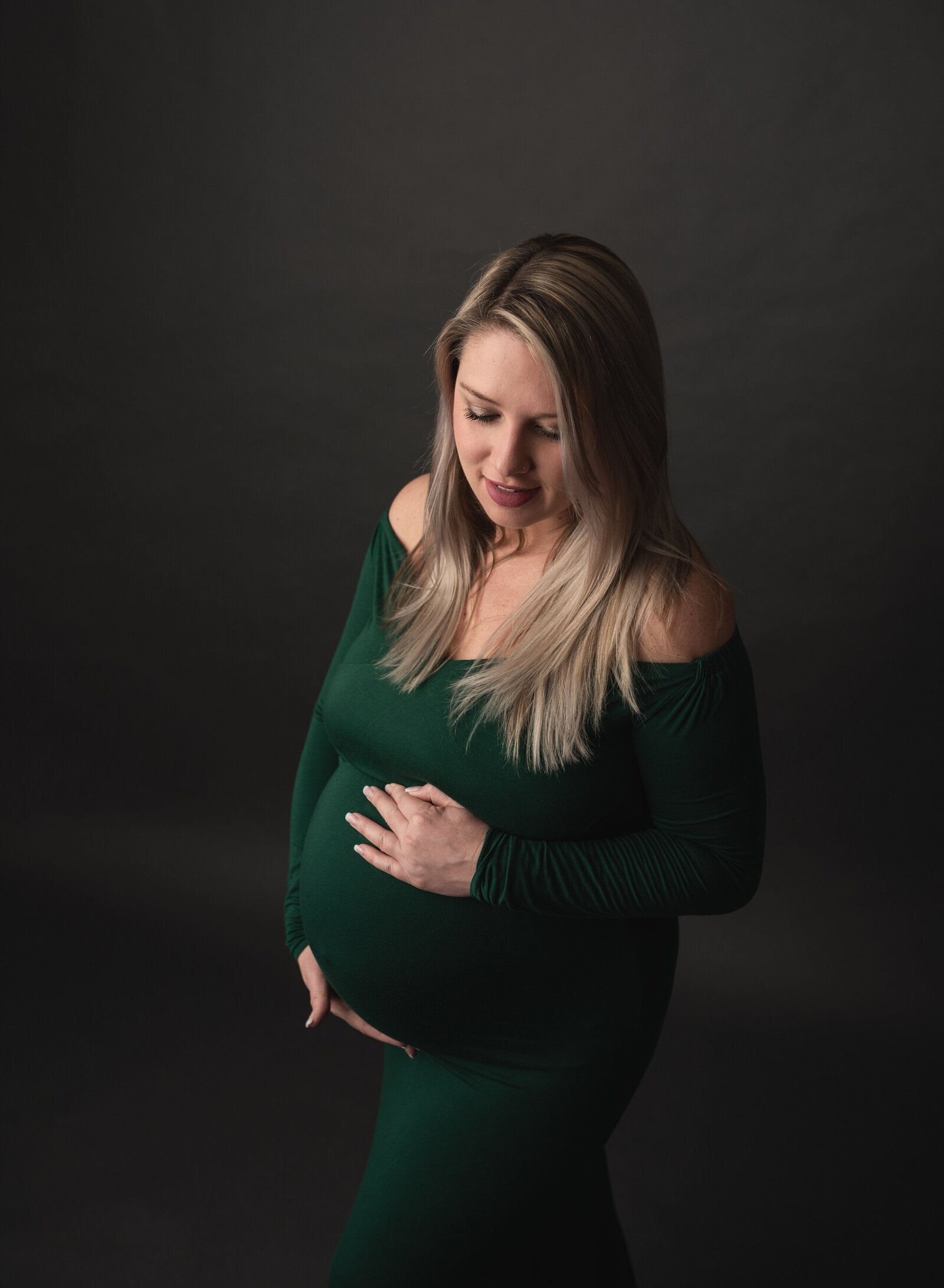 woman wearing a green gown for maternity pictures in a studio