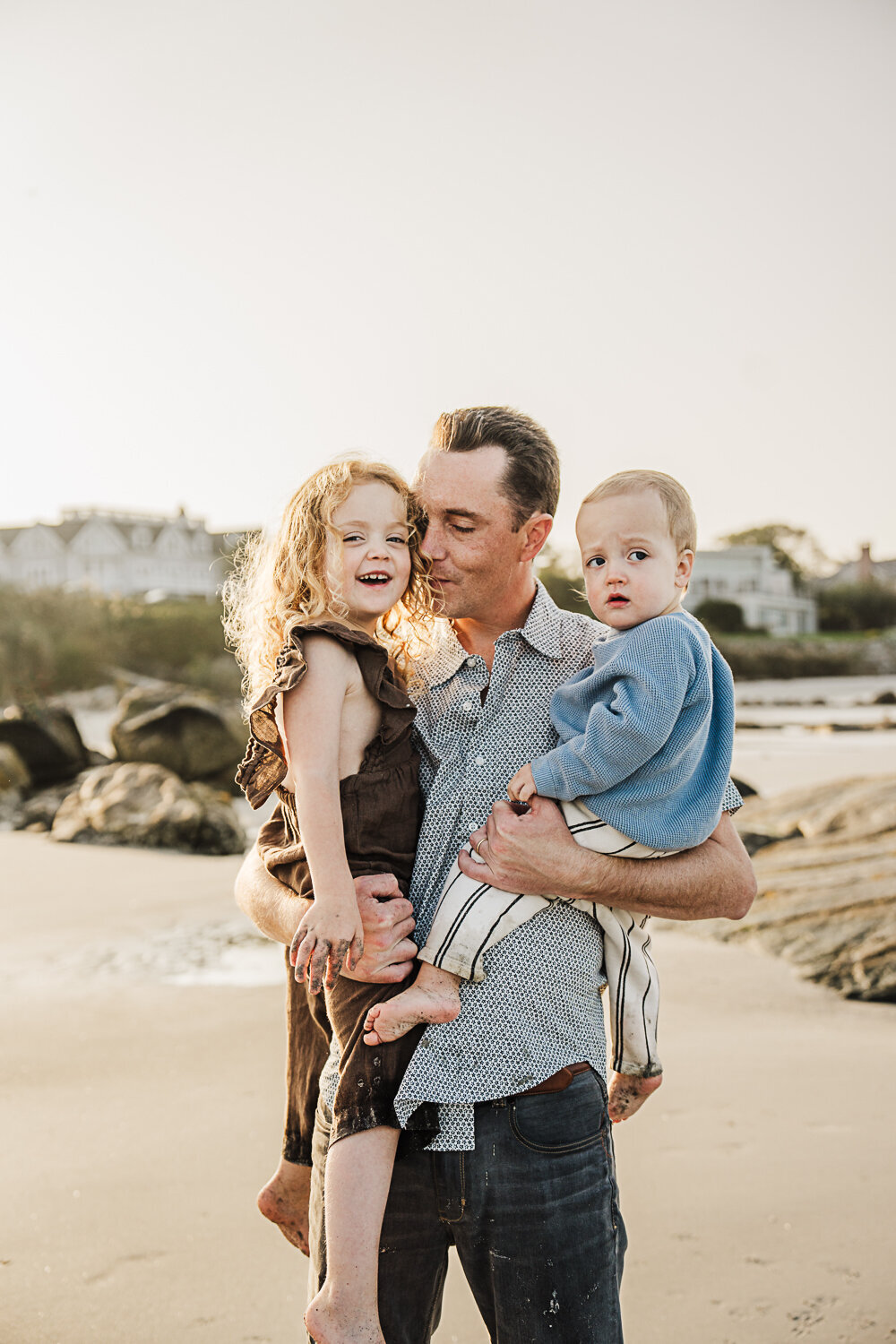 dad snuggles two kids in his arms at the beach