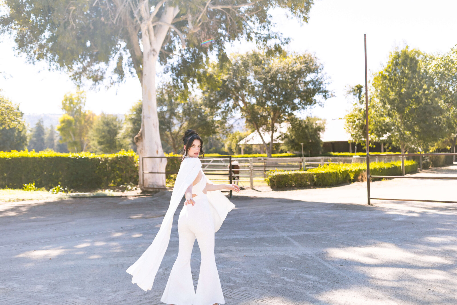 girl with dark hair wearing long flowy white outfit in front of a big tree