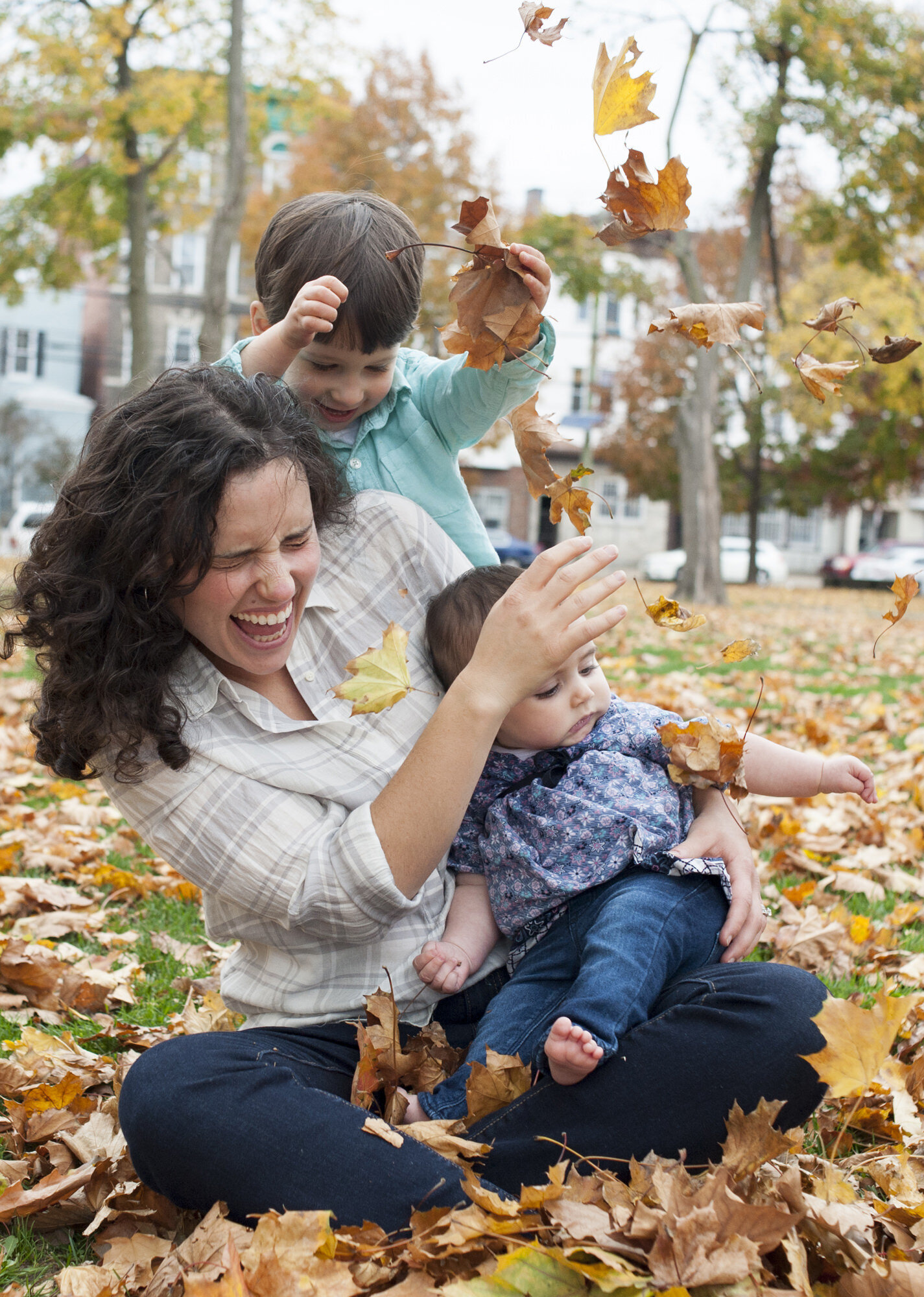 A parent throwing leaves and playing with two small kids 