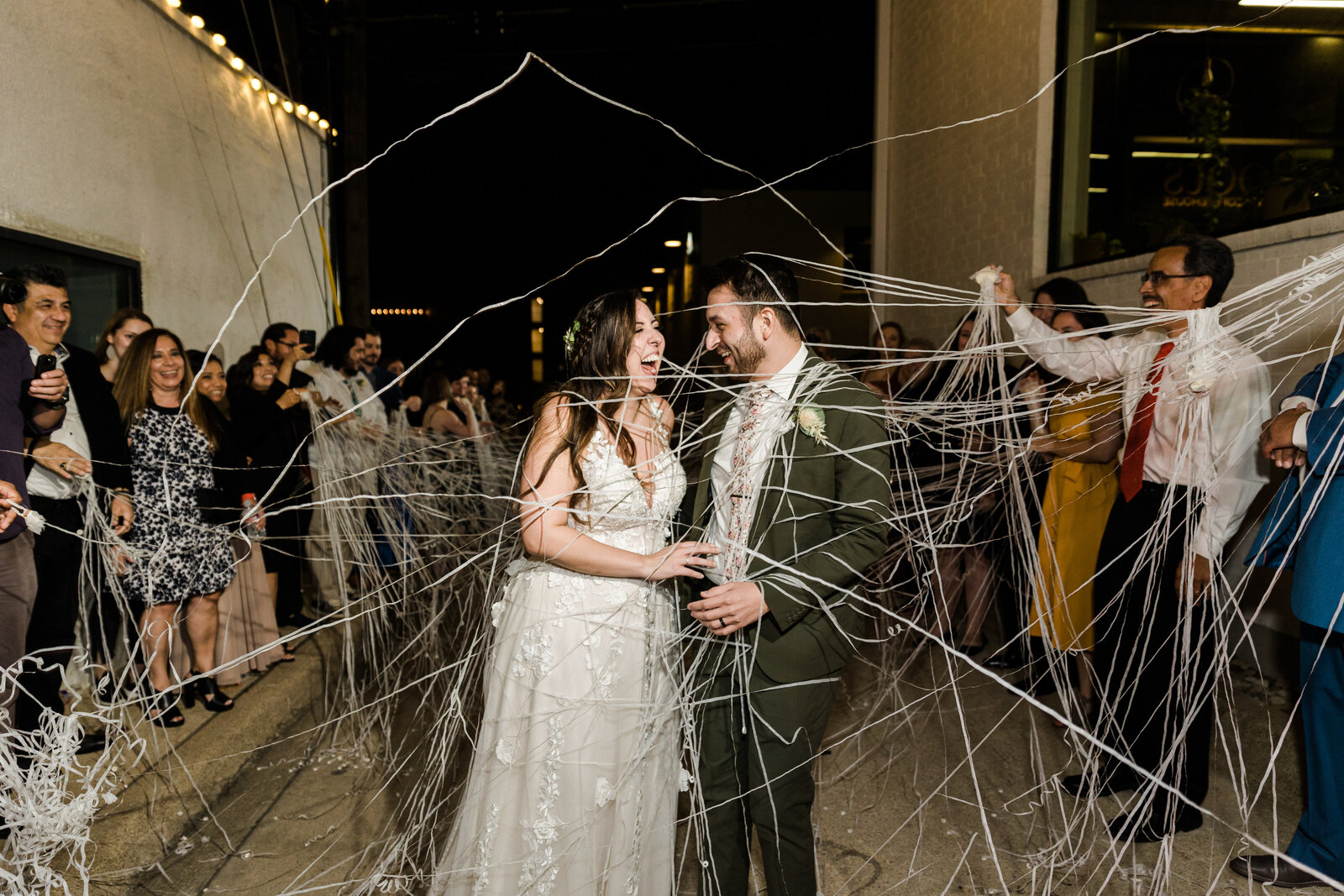 This is a wedding exit photo! A bride and groom are being showered with silver streamers by their guests, and it's at night. They're both laughing as the strings fly through the air.