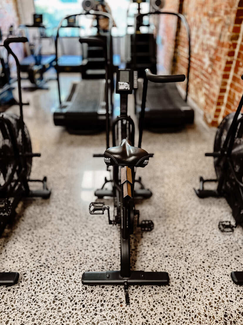 "Close-up of an Assault air bike in a Brunswick gym, positioned on polished concrete floors with cardio equipment and exposed brick walls in the background."