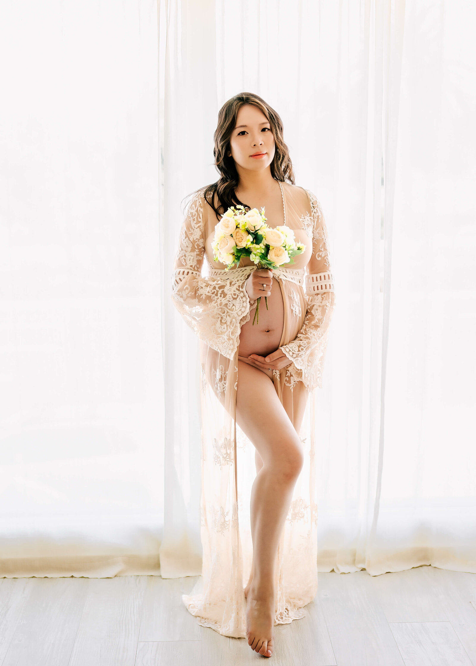 Expectant Mom wearing lace kimono and holding flowers during her studio maternity session by Ashley Nicole Photography.