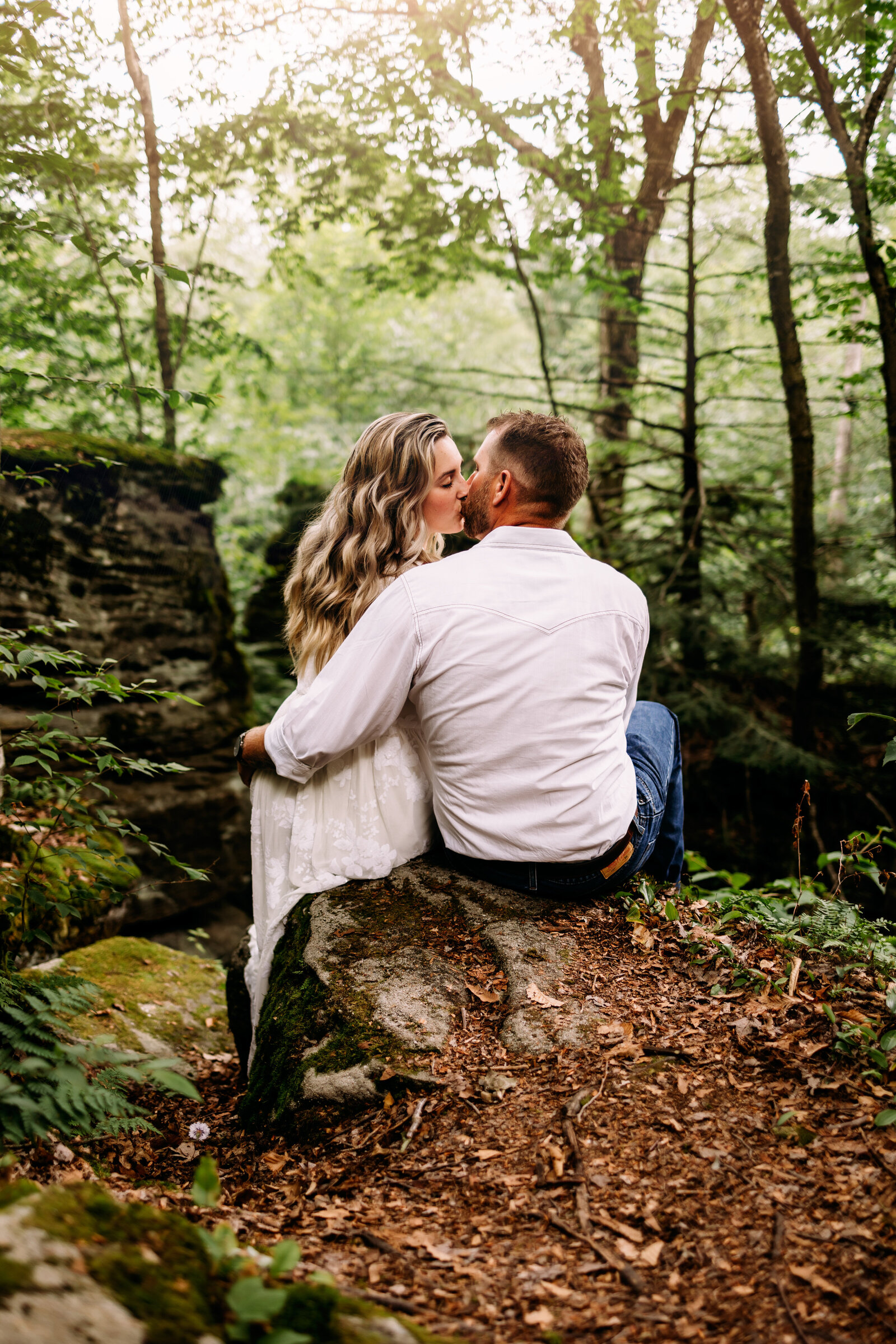Couple shares a kiss while sitting on the edge of a rock formation