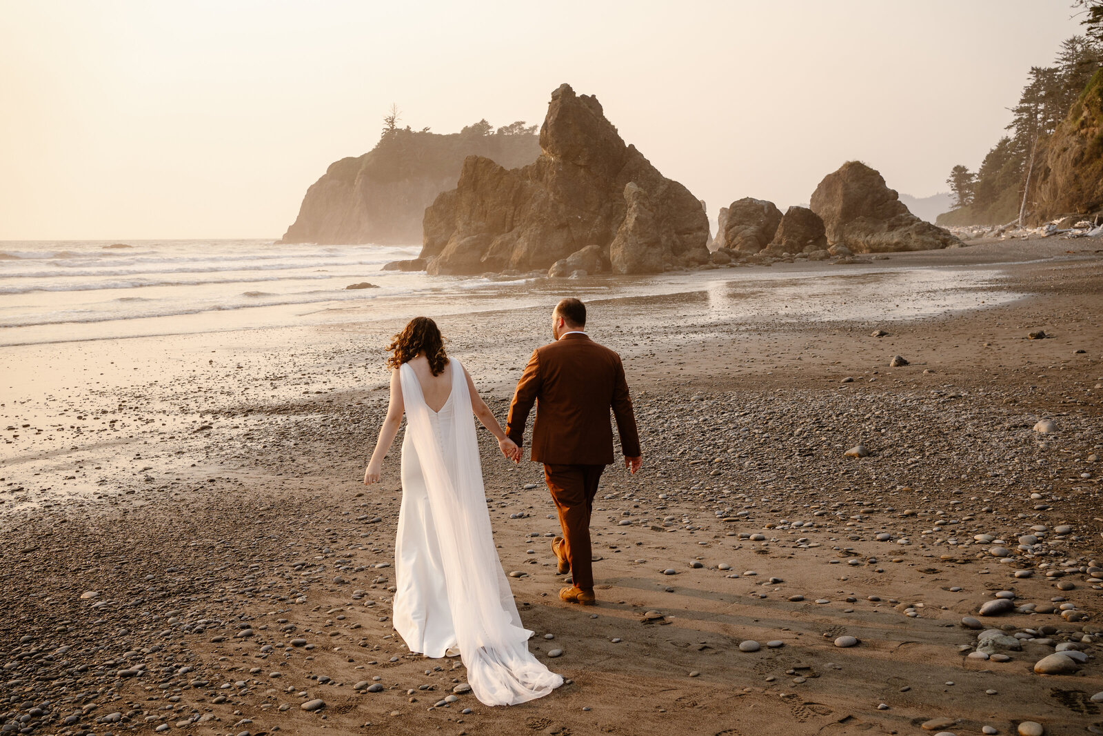 a bride and groom hold hands and walk off into the sunset on ruby beach during their washington elopement