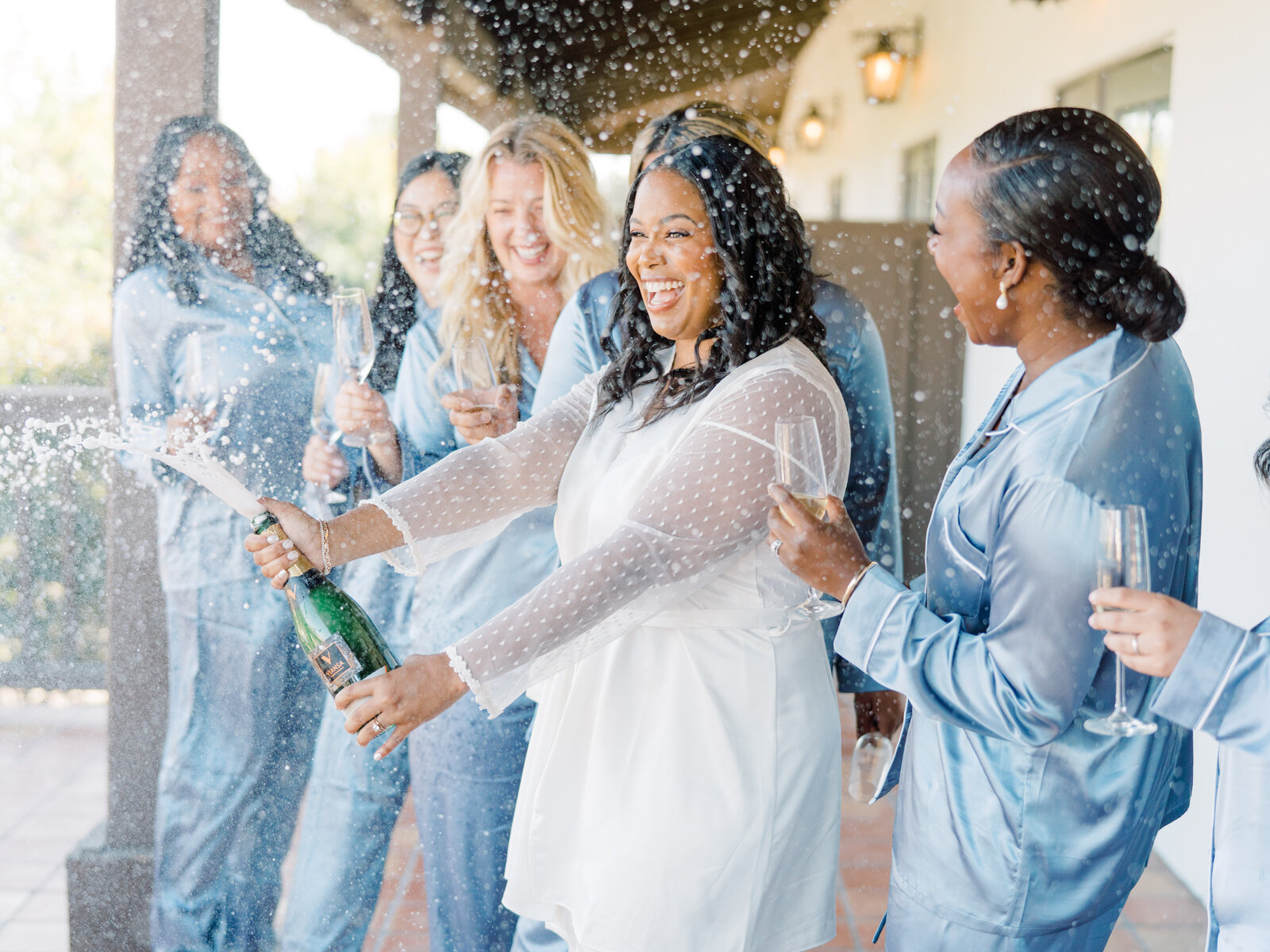 bride popping champagne to make a toast with her bridesmaids