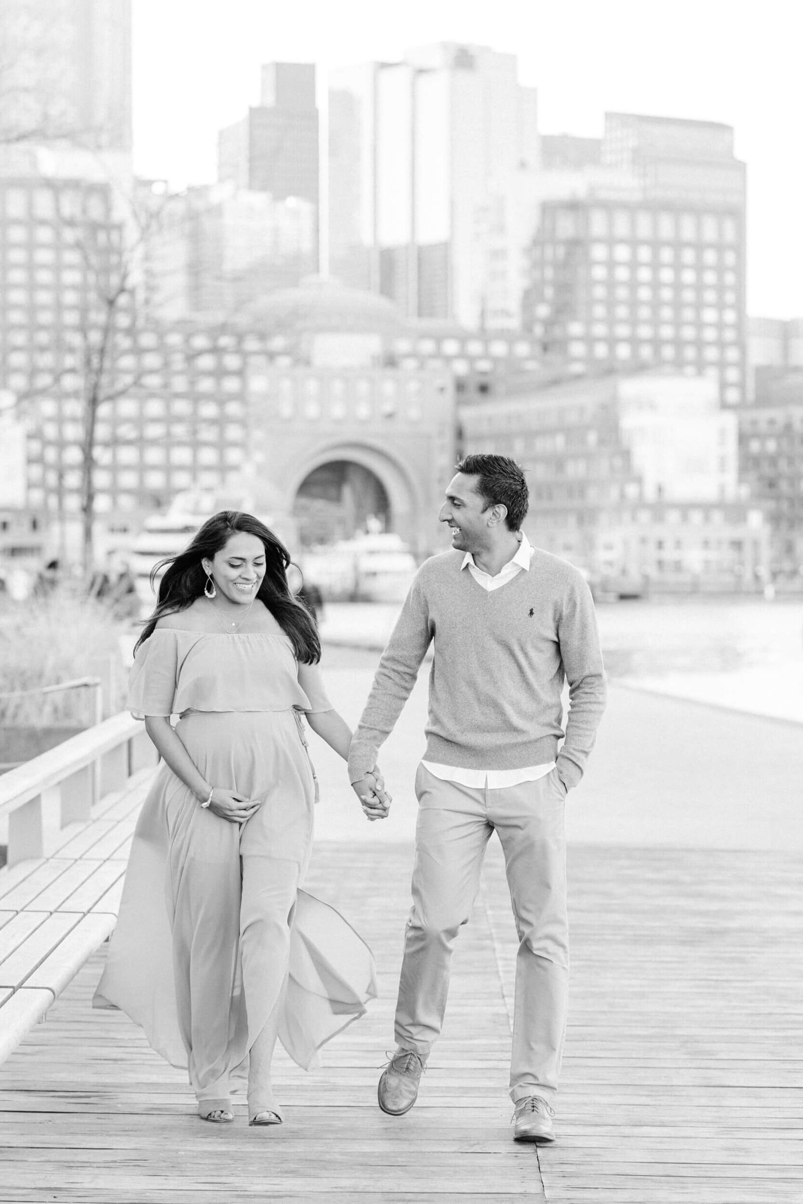 Black and white, pregnant woman and her husband walk along the pier at Boston Seaport