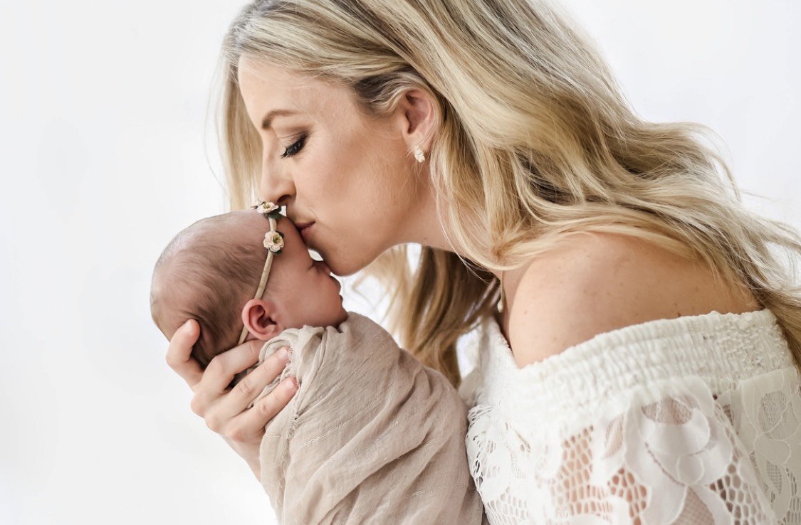 Woman kissing newborn baby's forehead with eyes closed.