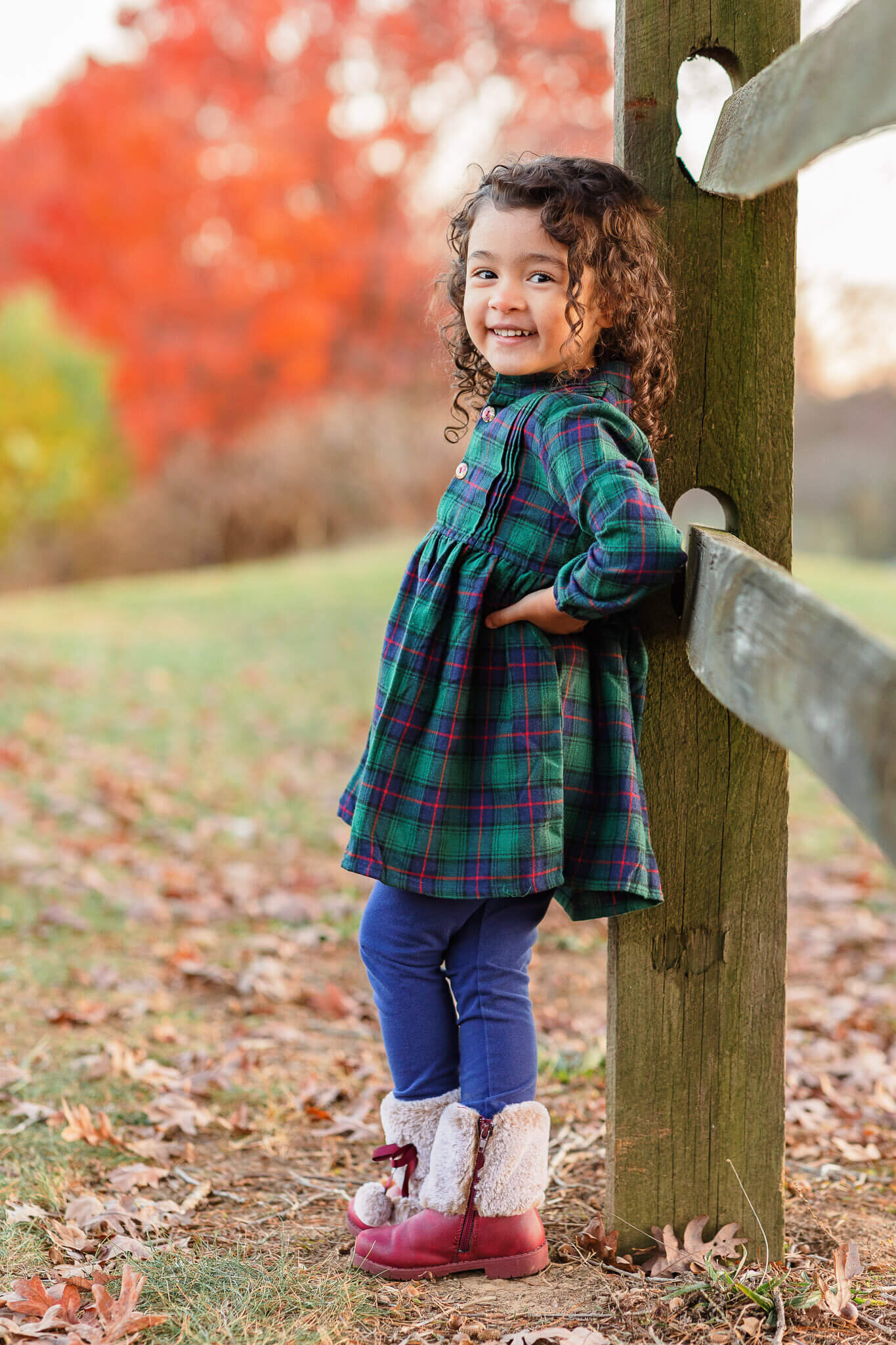 A little girl in green leaning up against a fence