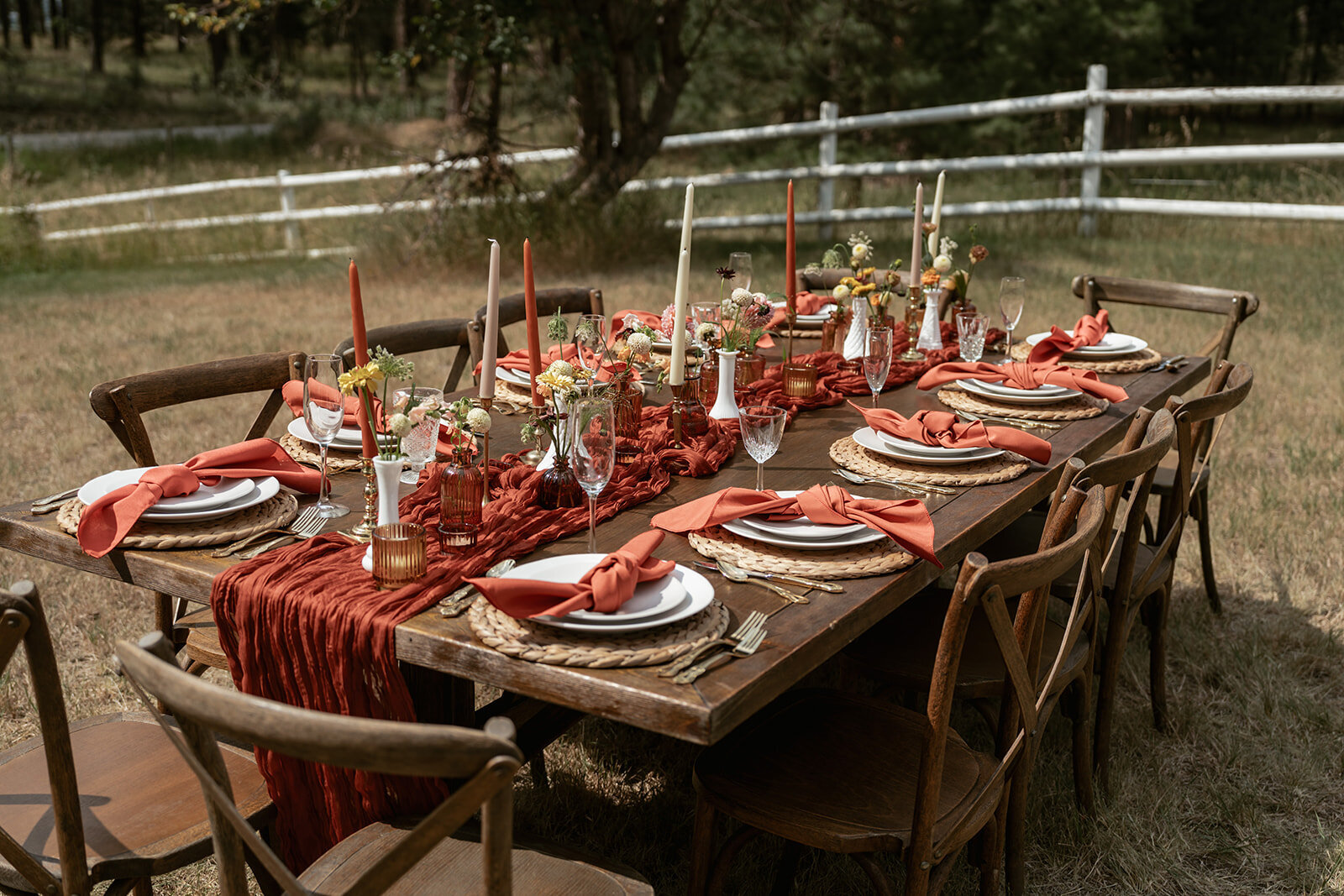 Warm outdoor elopement table design with rust-colored napkins, woven chargers, and taper candles styled for an intimate fall celebration.