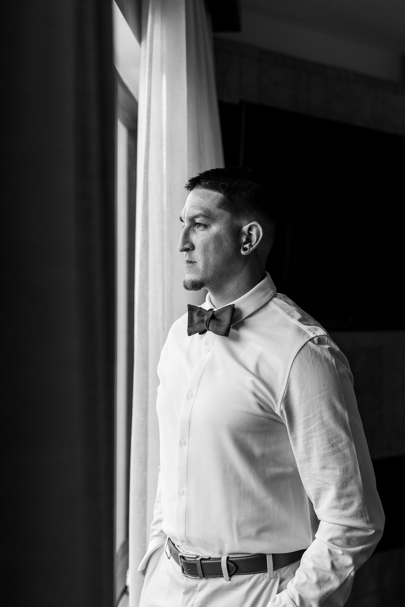 Black and white image of the groom looing out the window before his wedding in Moab Utah