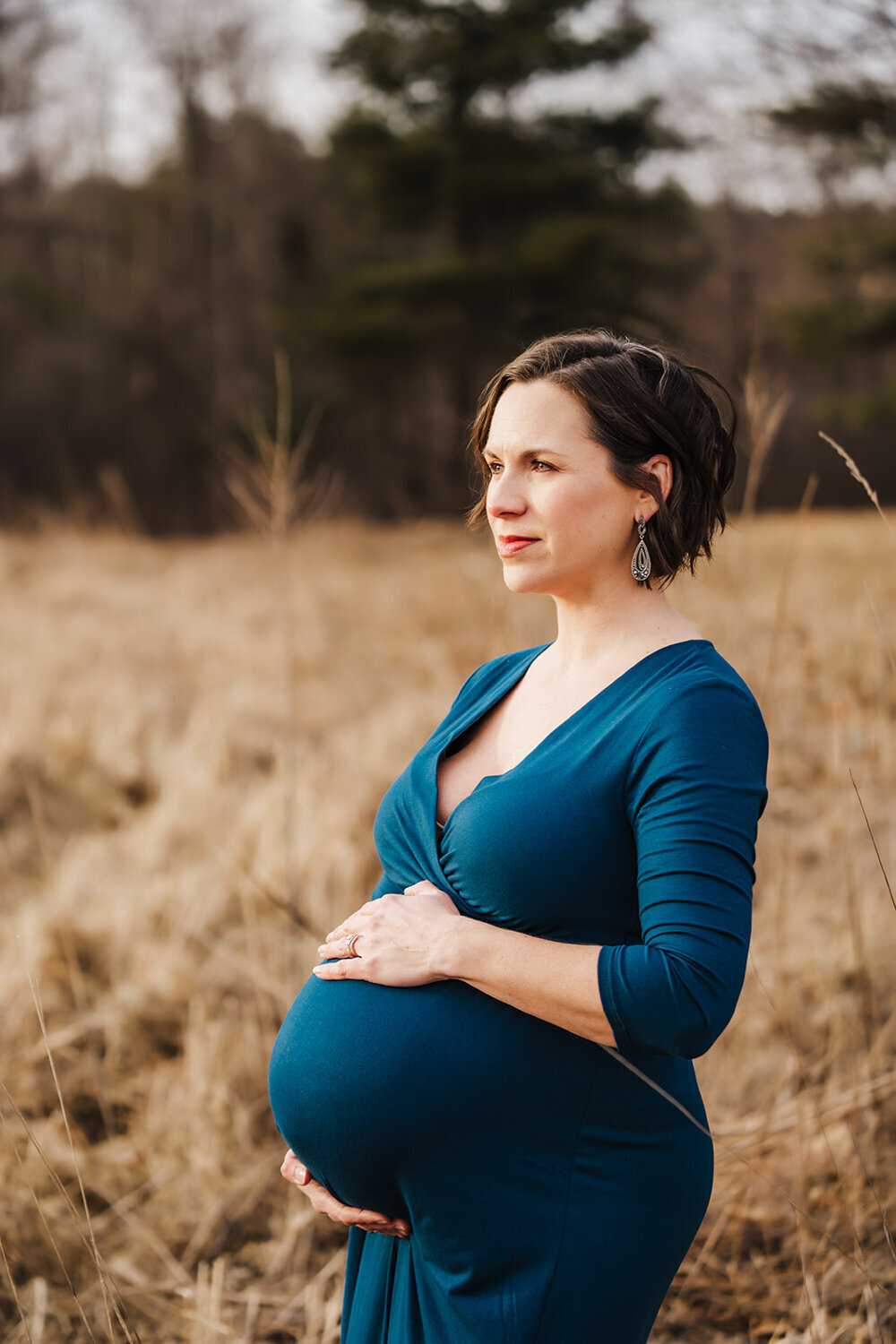 pregnant mom in blue dress stands in profile at sunset
