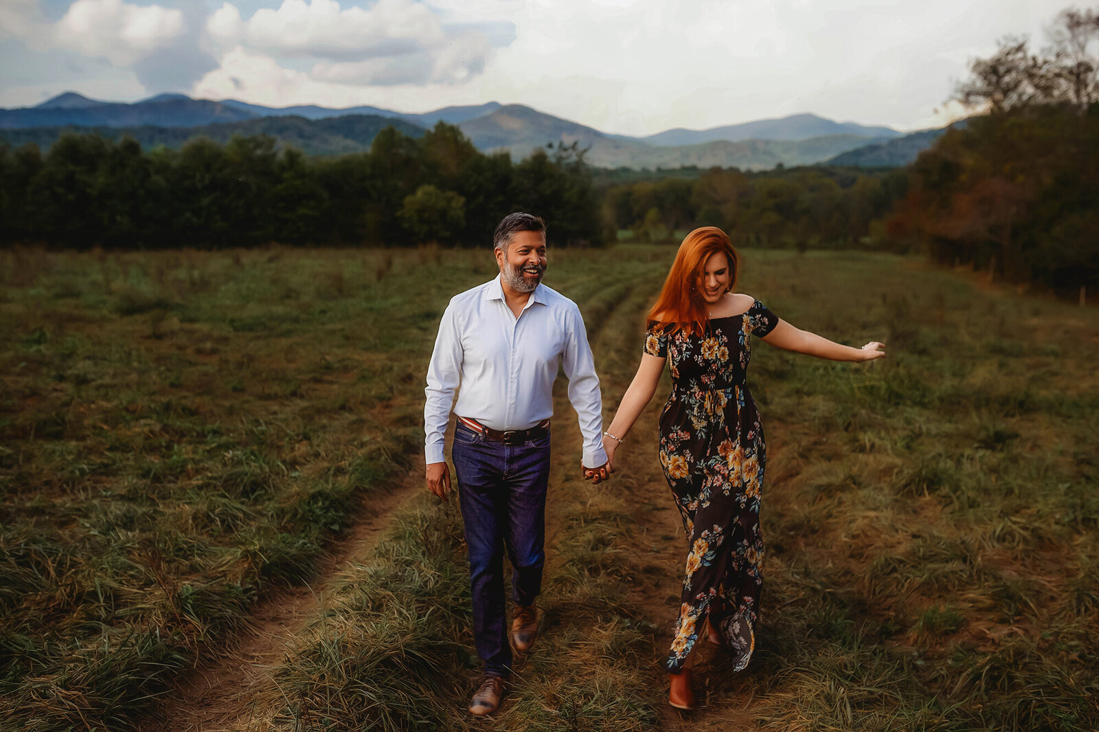 An engaged couple walks hand in hand during  Engagement Photos in a mountain field in Asheville, NC.