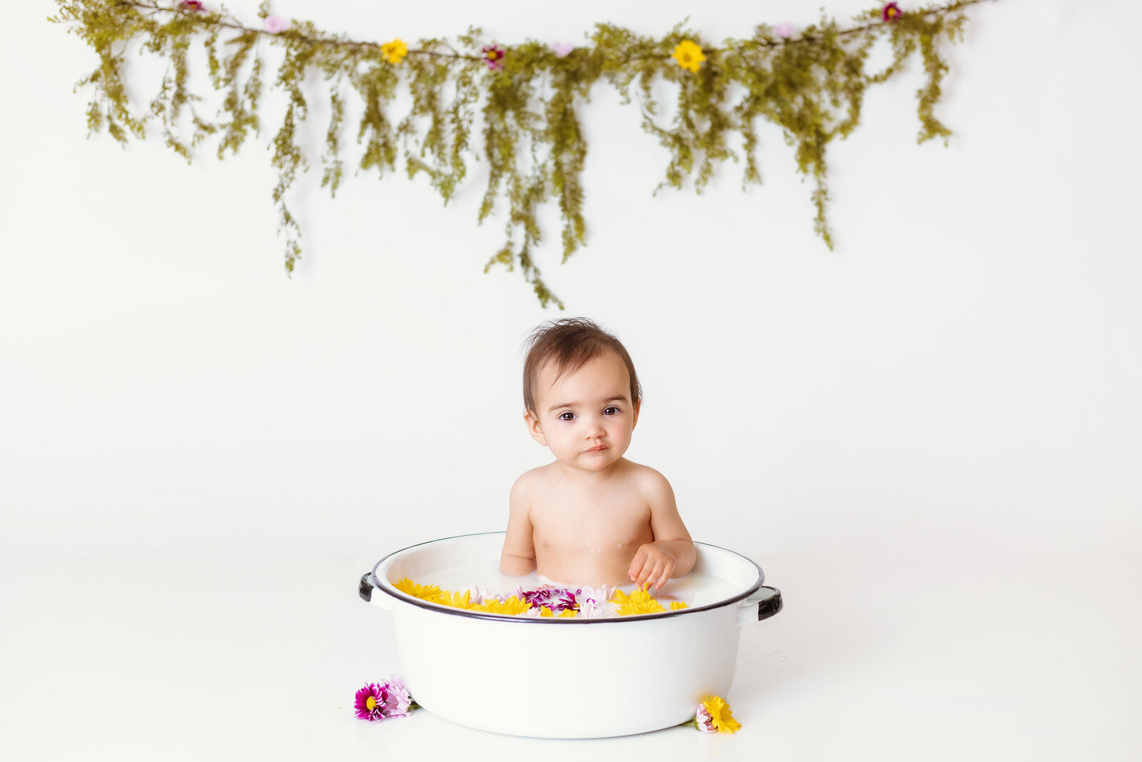 Milestone Photographer, a baby takes a milk bath in a ceramic pot