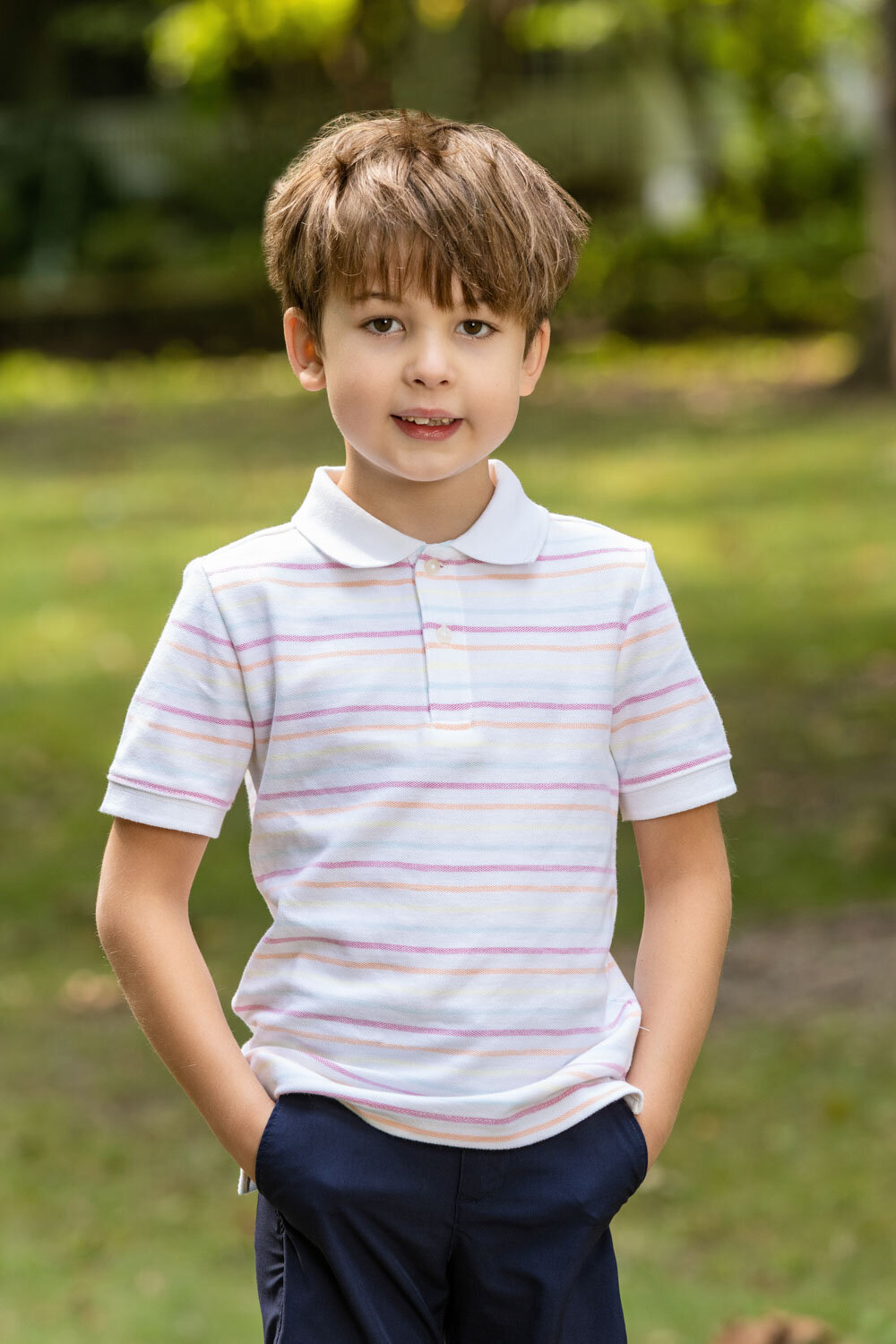 A young boy wearing a white and pink striped polo shirt