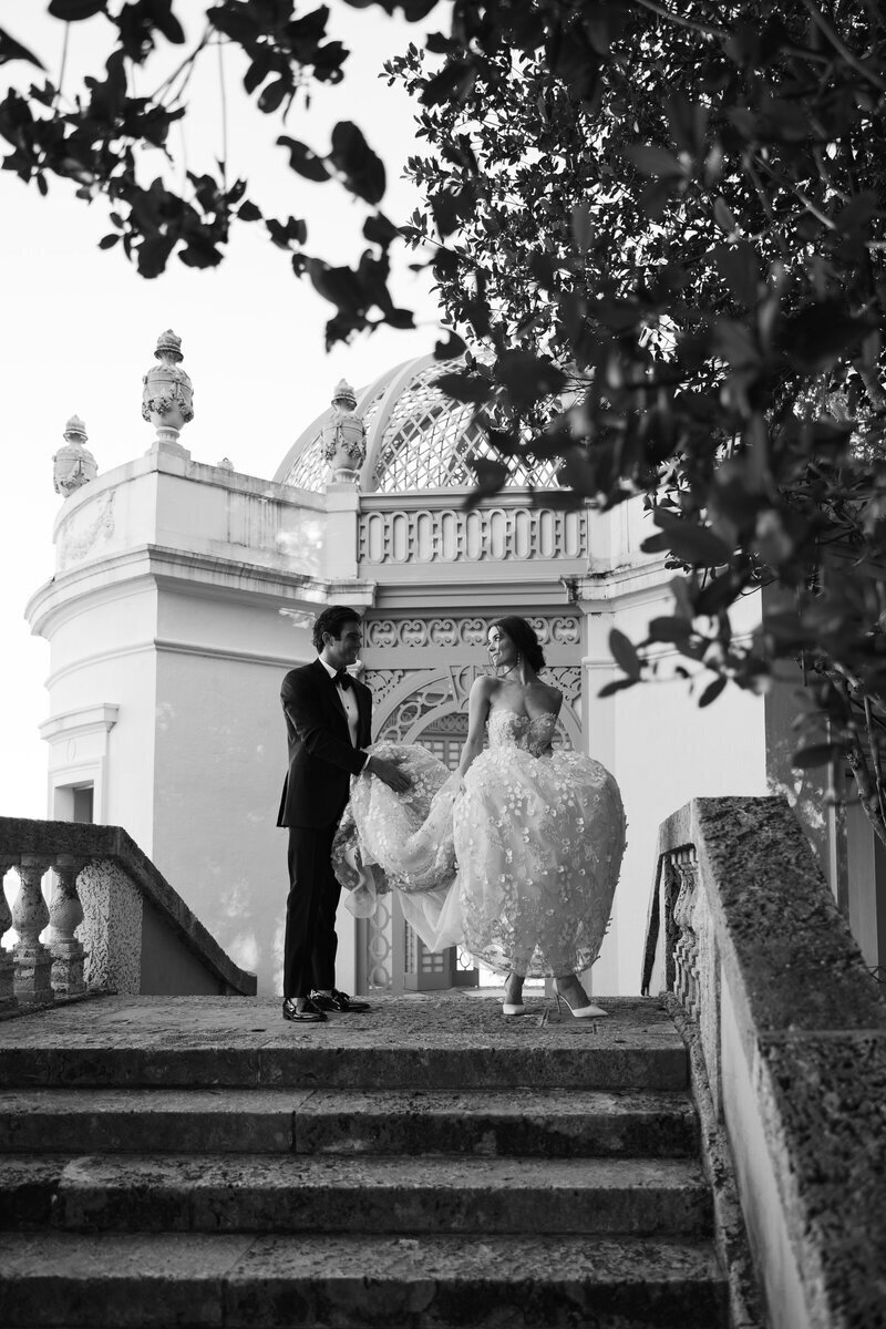groom holding bride's dress walking down stairs, taken by fort myers florida wedding photographer