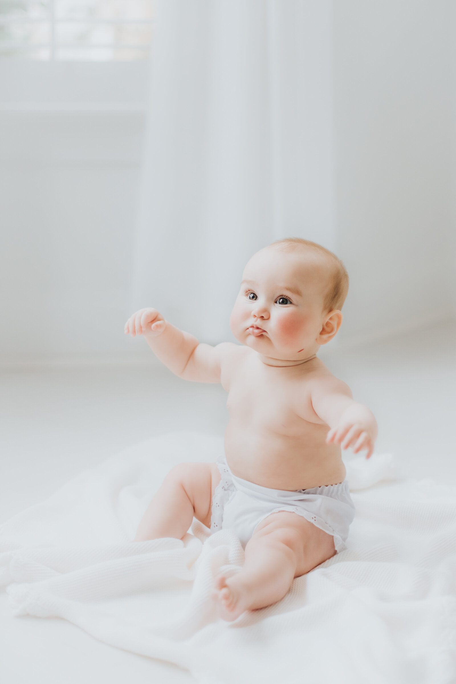 Baby girl in white diaper cover sits up during baby session in Raleigh NC studio