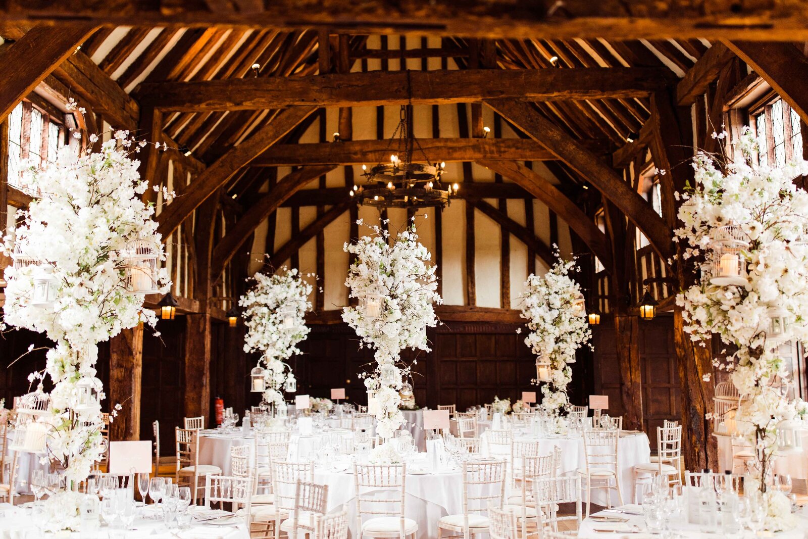 Tall, glamorous white floral centrepieces decorating a rustic barn wedding reception venue in Hampshire.