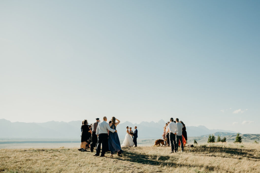grand teton elopement with bride adn groom holding hands and getting married with their friends and family surrounding them with the Tetons in the distance captured by jackson hole photographers