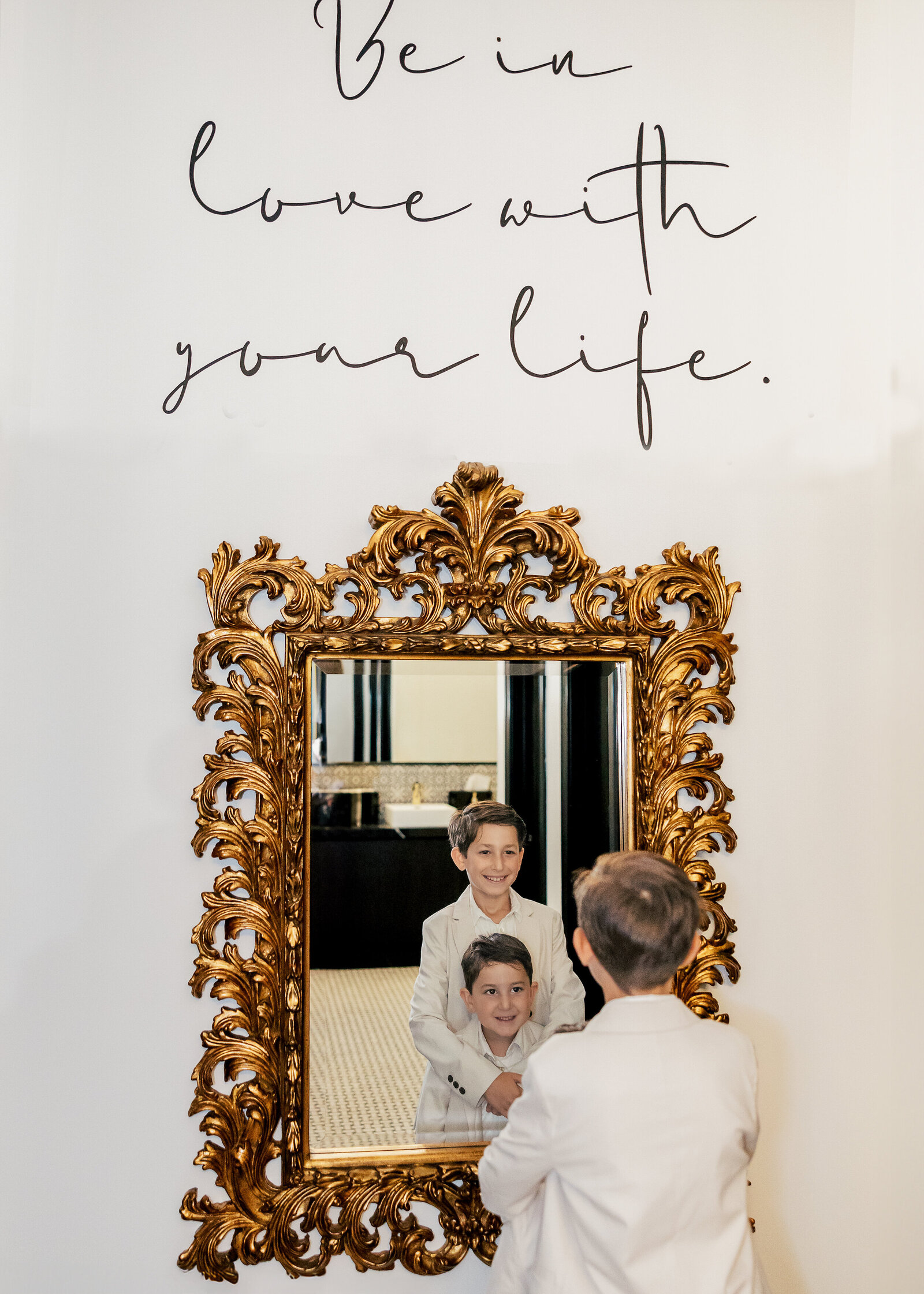 Brothers look at their reflection in an ornate mirror in an event space.
