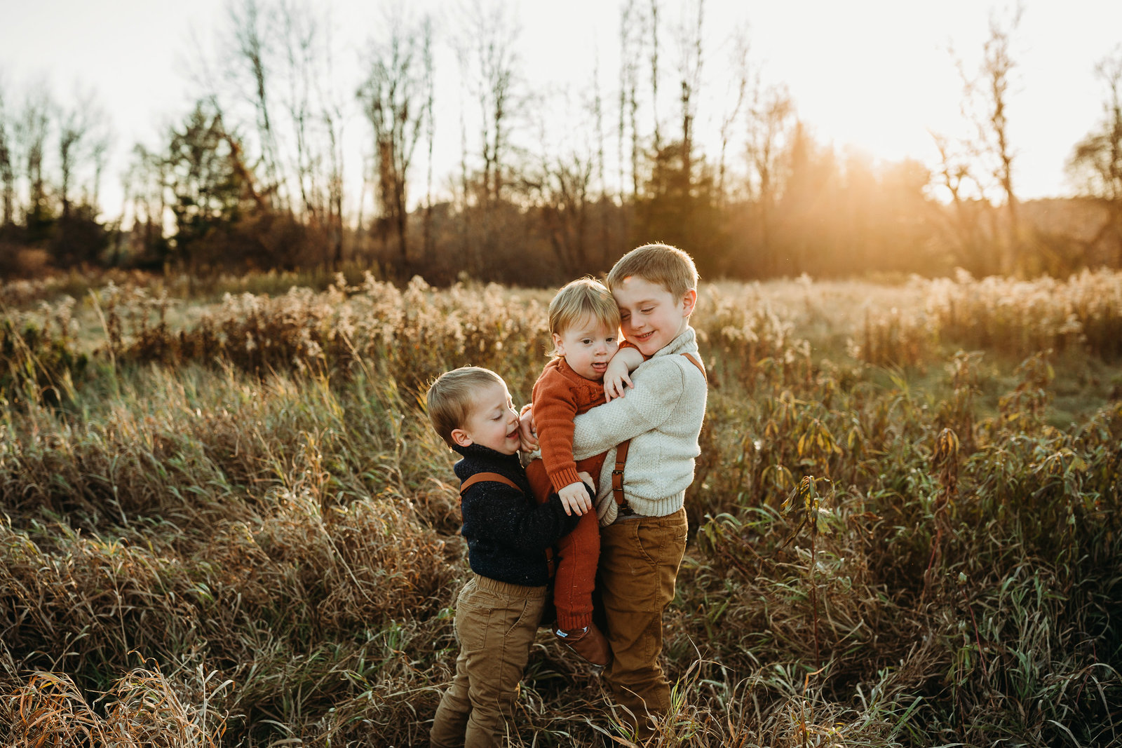 three brothers embrace in a field at sunset for family photos