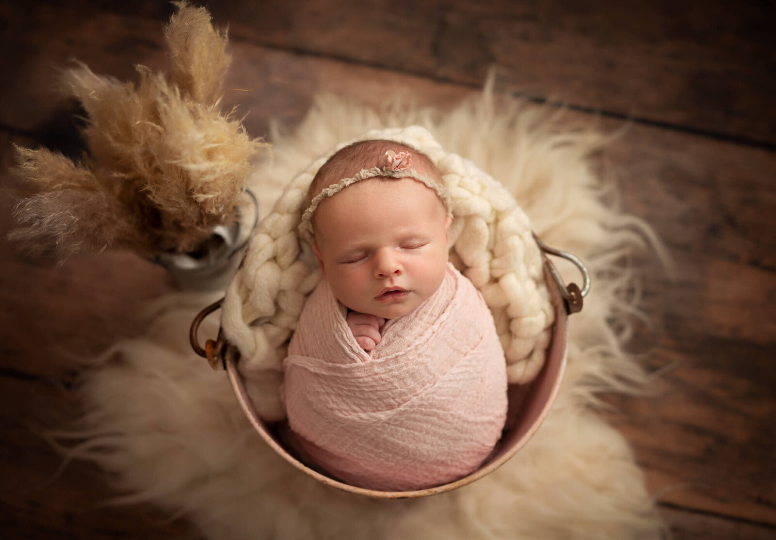 Sleeping newborn girl in pink wrap with pampas grass