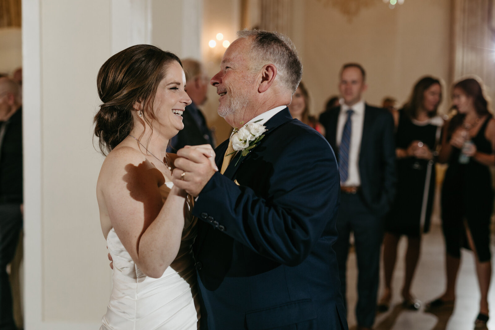 A bride dances with her father at a wedding reception in a ballroom