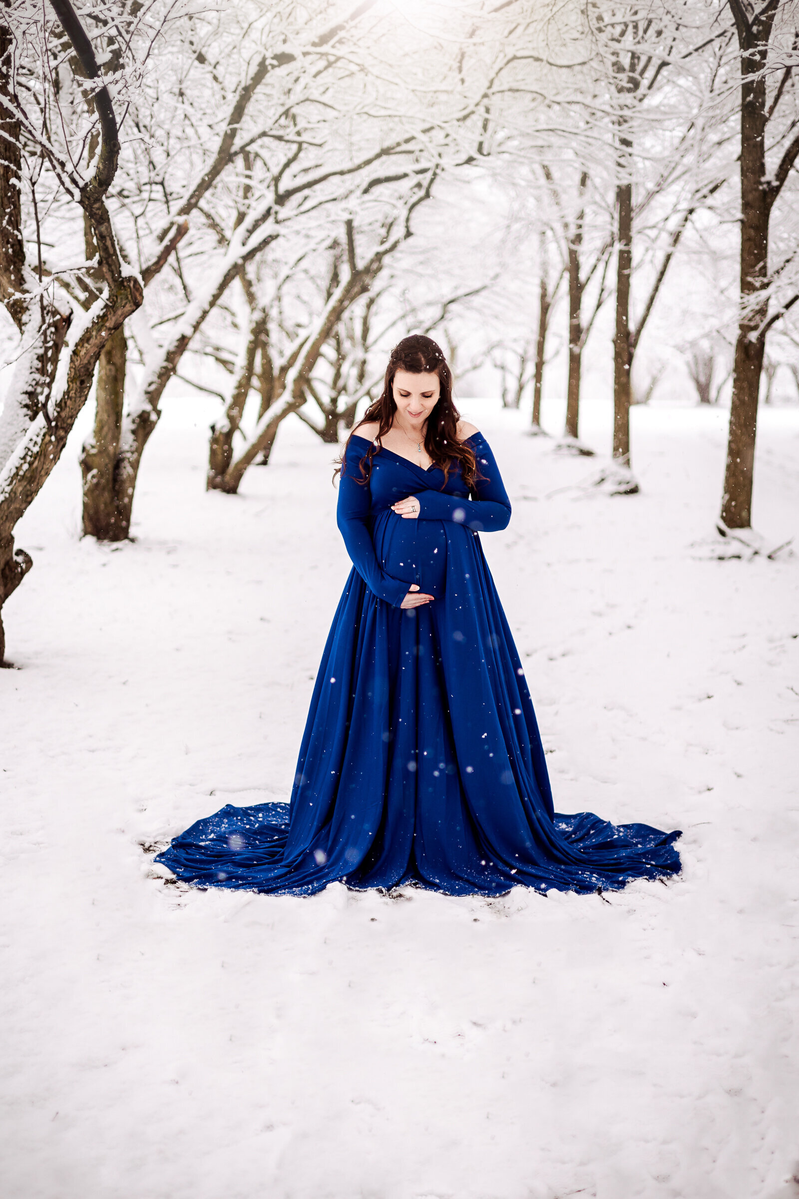 Pregnant woman in blue dress holds her belly on a snowy day in Erie, PA