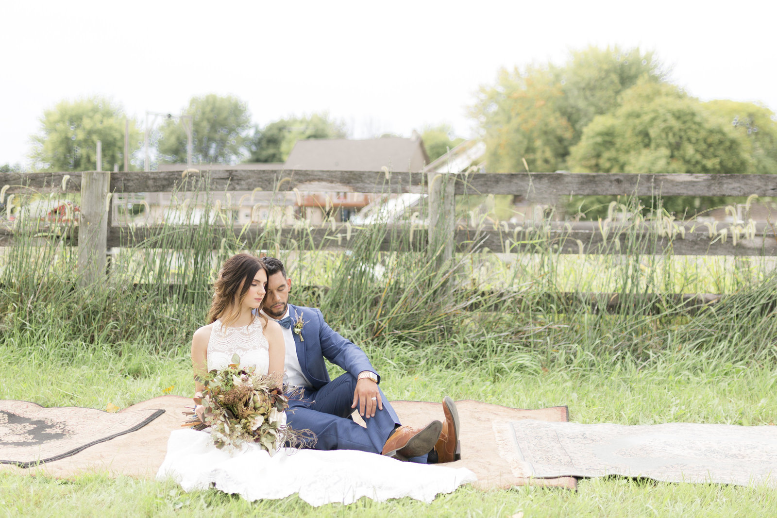 Bride and groom snuggle on a blanket in front of a fence; Bear Cave Lake