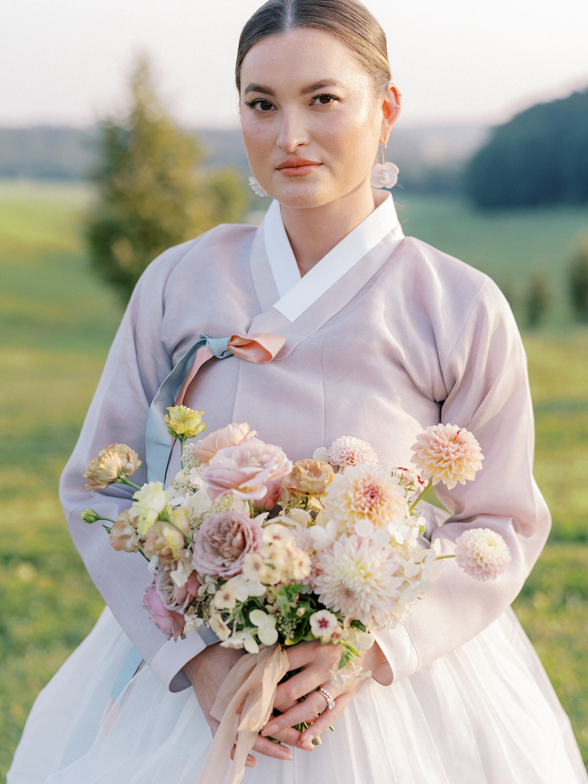 Portrait of the bride in traditional Korean hanbok holding bridal bouquet including blush garden roses, taupe garden roses, blush dahlias, peach dahlias, peach lisianthus, phlox, and white hydrangea.