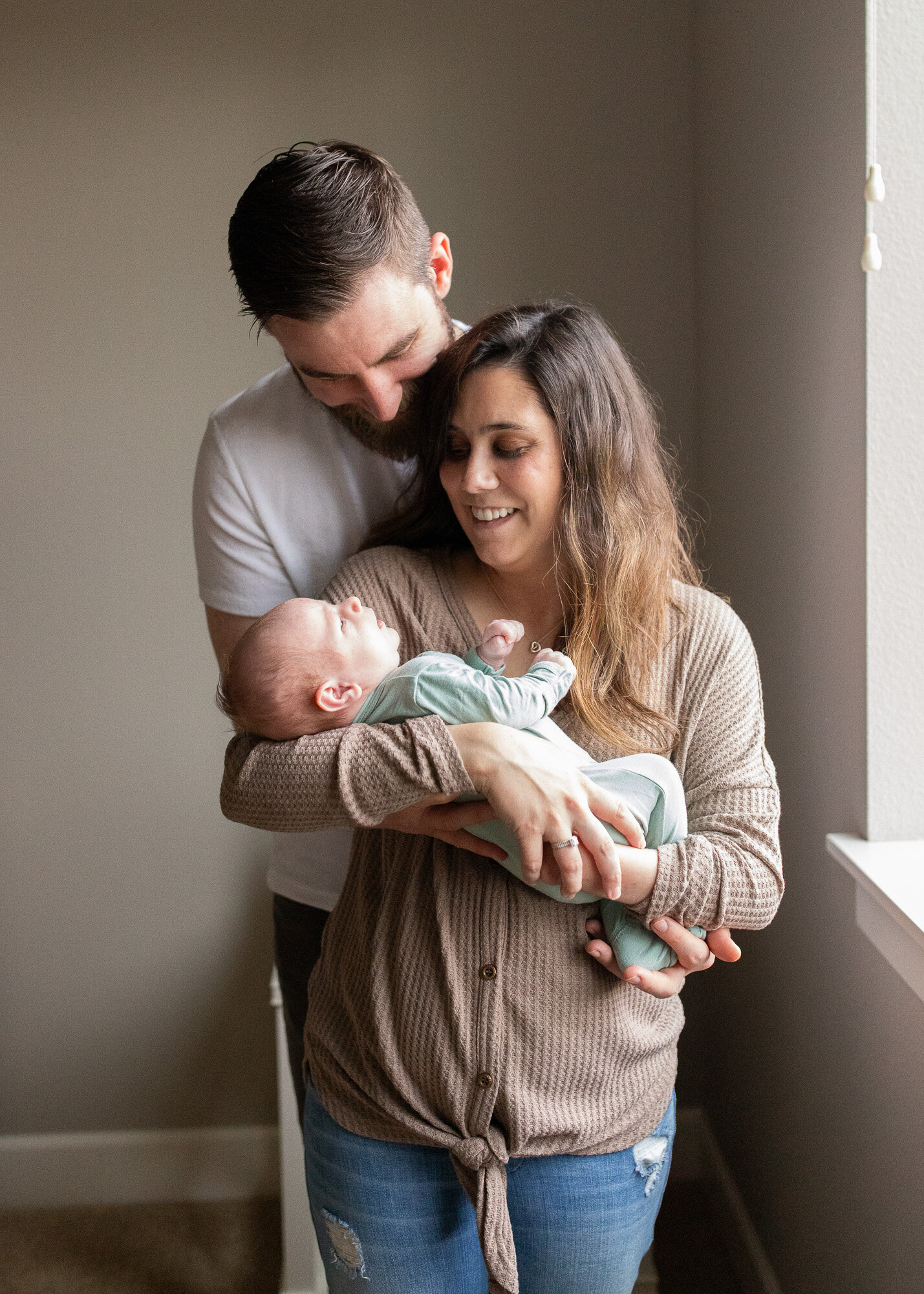 New parents loving on their newborn son by naturally lit window.
