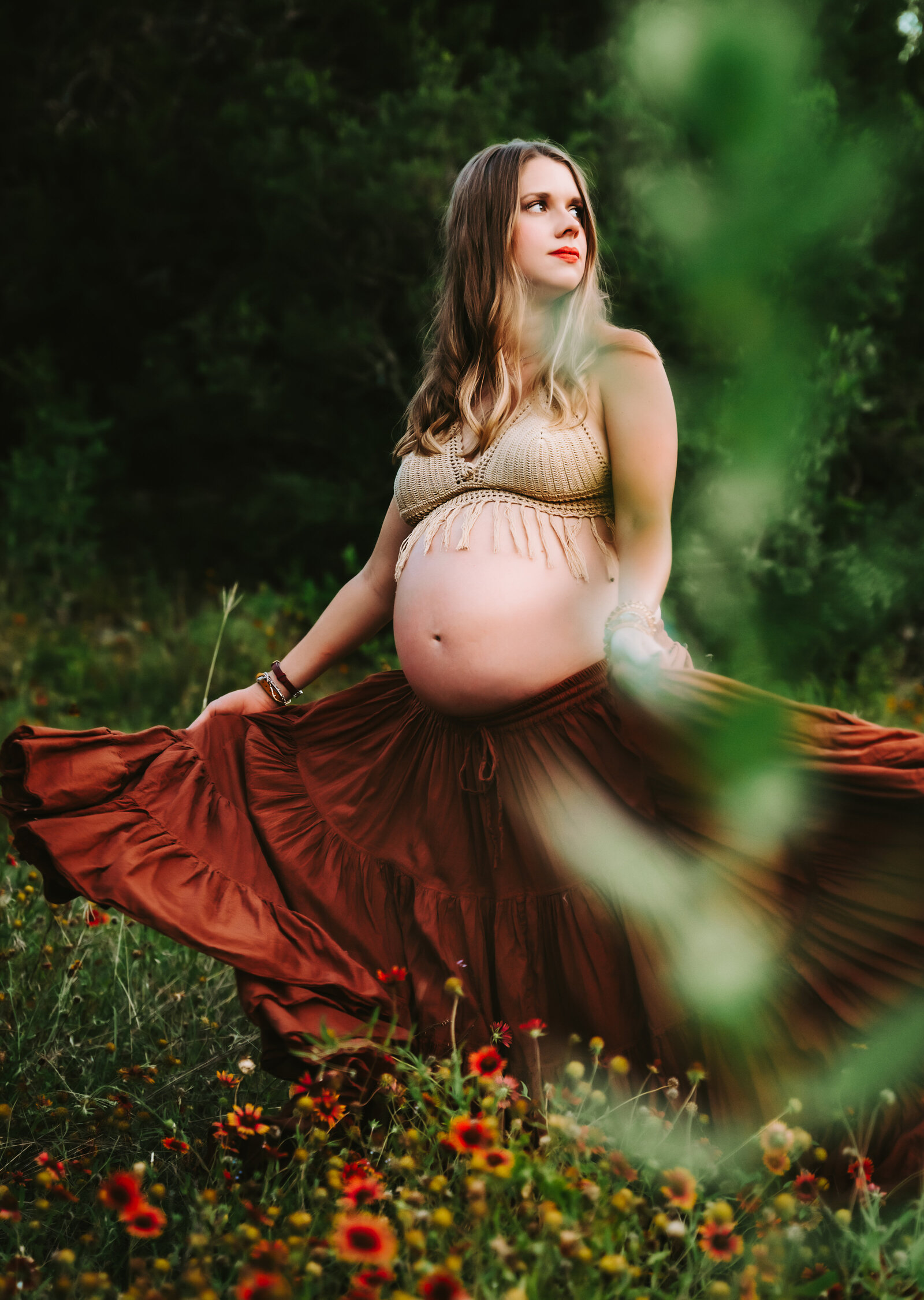 Maternity Photographer, a pregnant woman holds her skirt and spins in a flower field