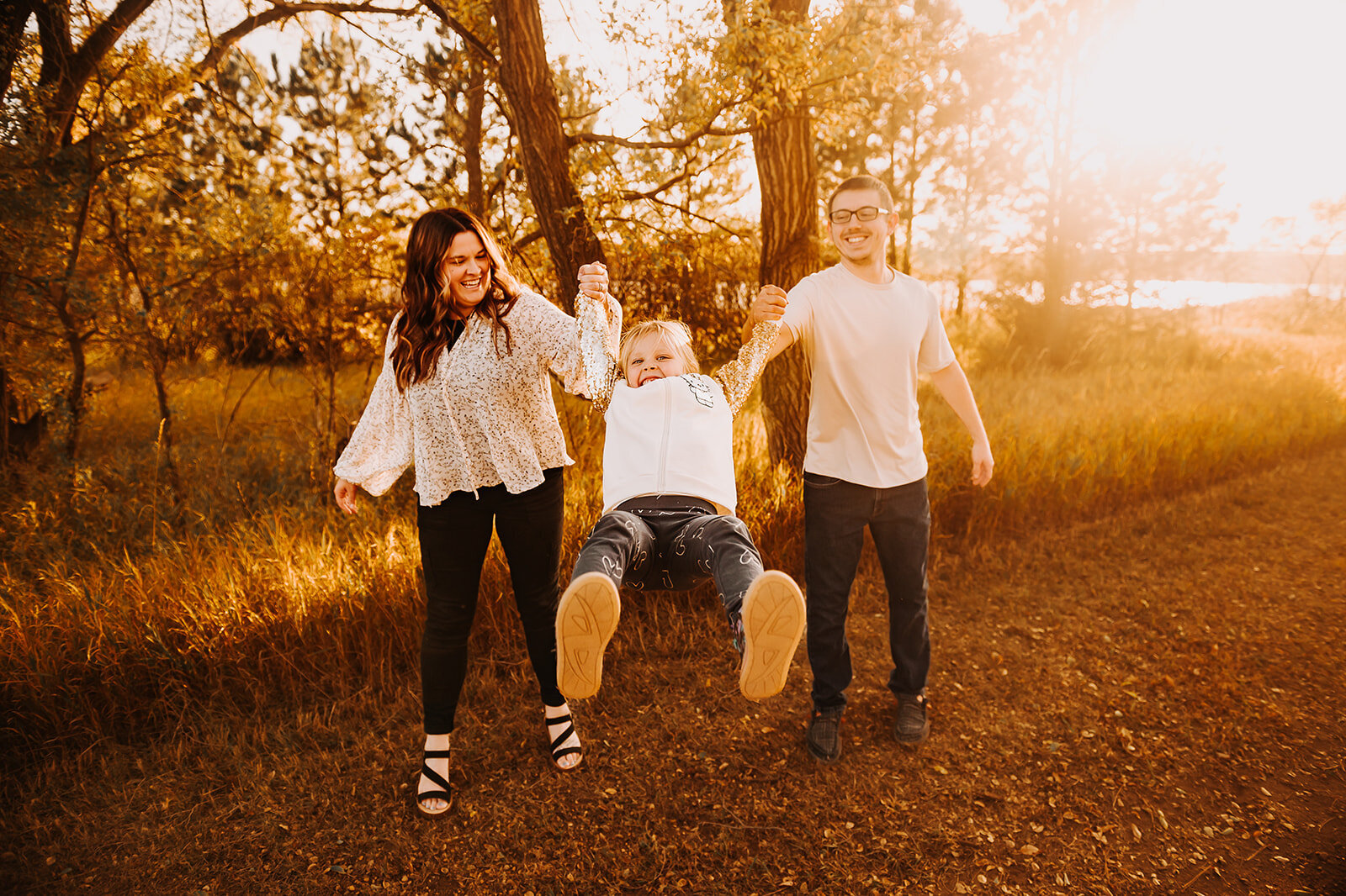 With the fall sun dropping to give the golden glare, a family has fun swinging and being silly together during their family mini session at Sweet Briar Lake. 