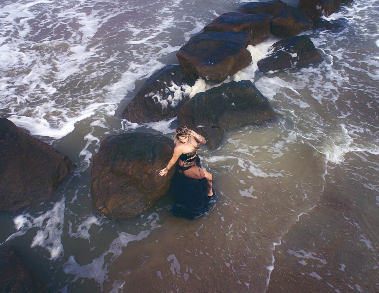 Aerial shot of woman on beach with black gown  by rocks