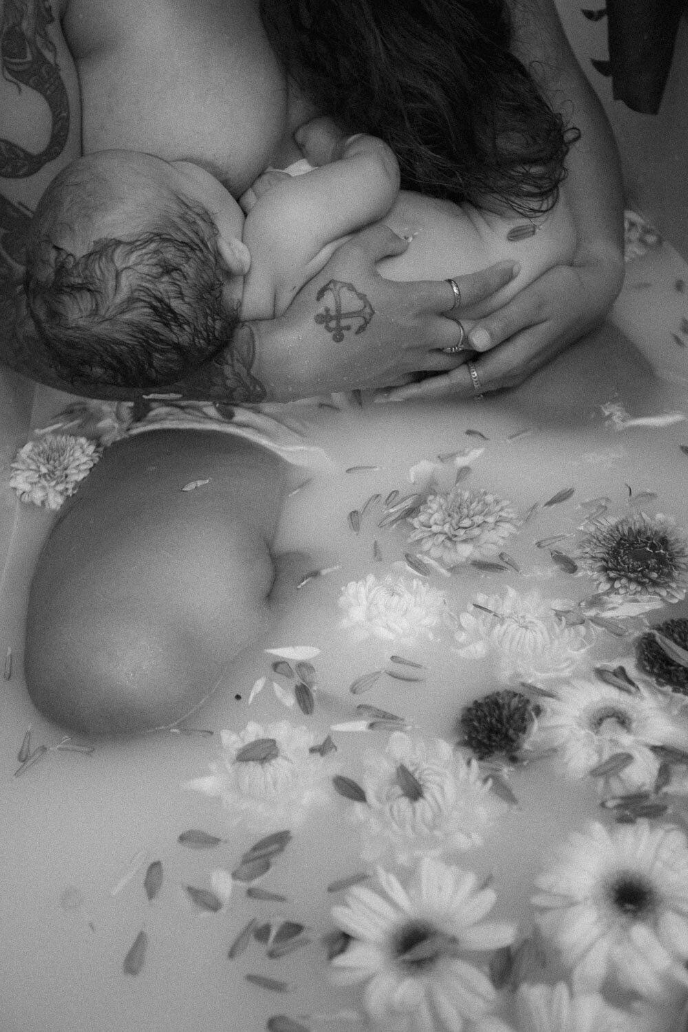 Black and white photo of a mother breastfeeding her baby in a milk bath adorned with flowers