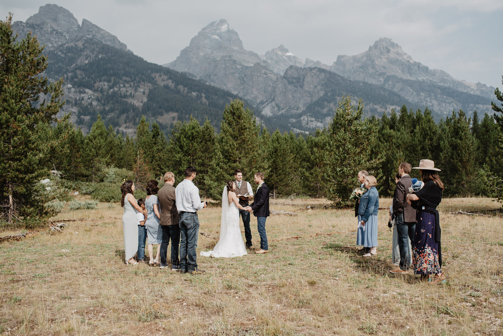 wyoming elopement captured by jackson hole photographers with bride adn groom holding hands and getting married in a meadow in front of a wood at the base of the grand teton mountains