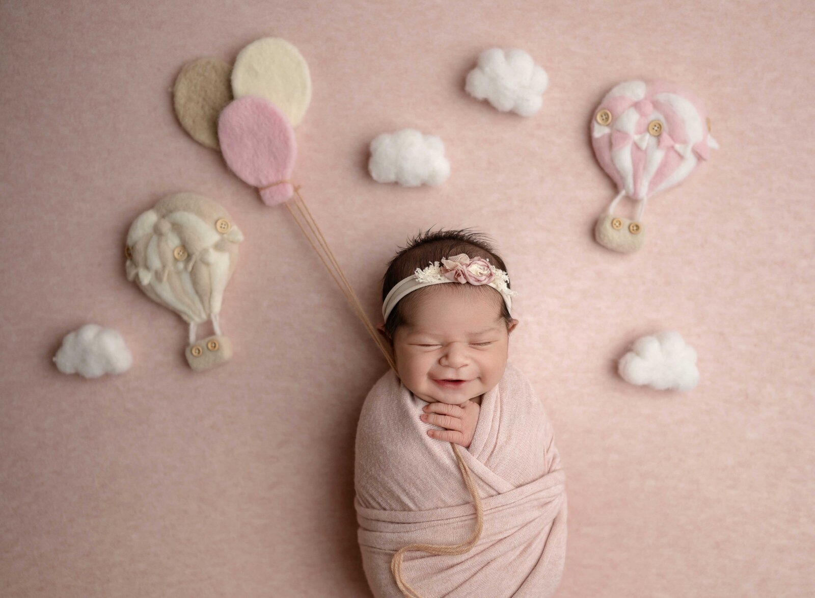 Baby girl holding felted balloons and smiling in her sleep. Photographed at Atlanta newborn photo studio.