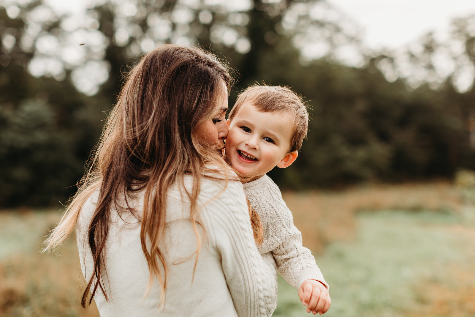 boy peeks over moms shoulder and laughs during family photos in belmont