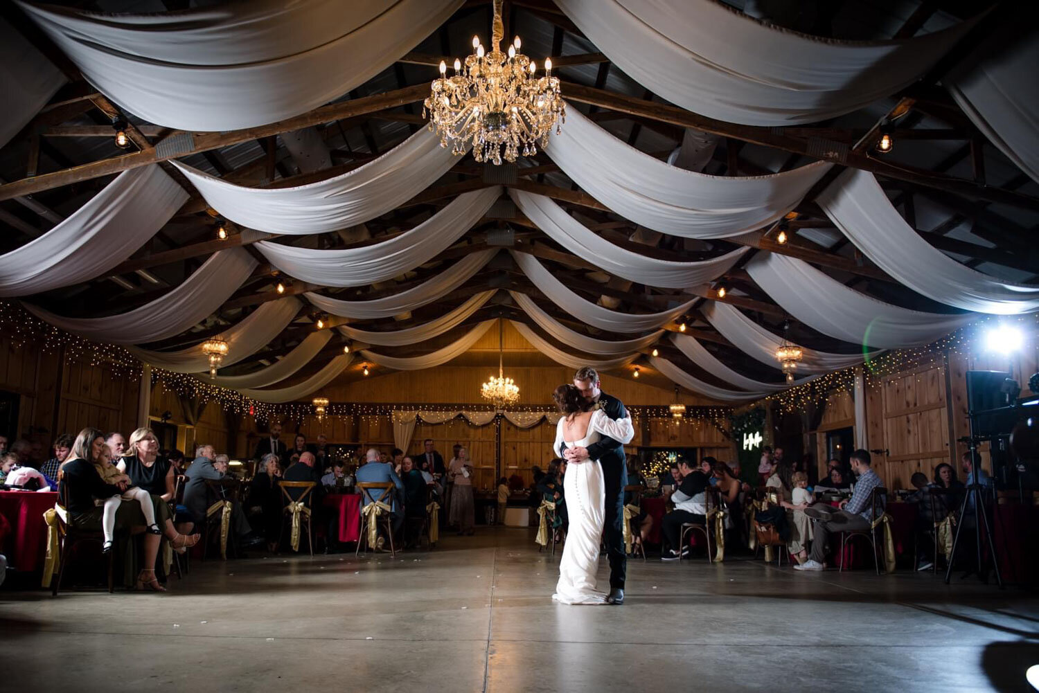 First dance under draped fabric and chandelier lighting in a rustic venue