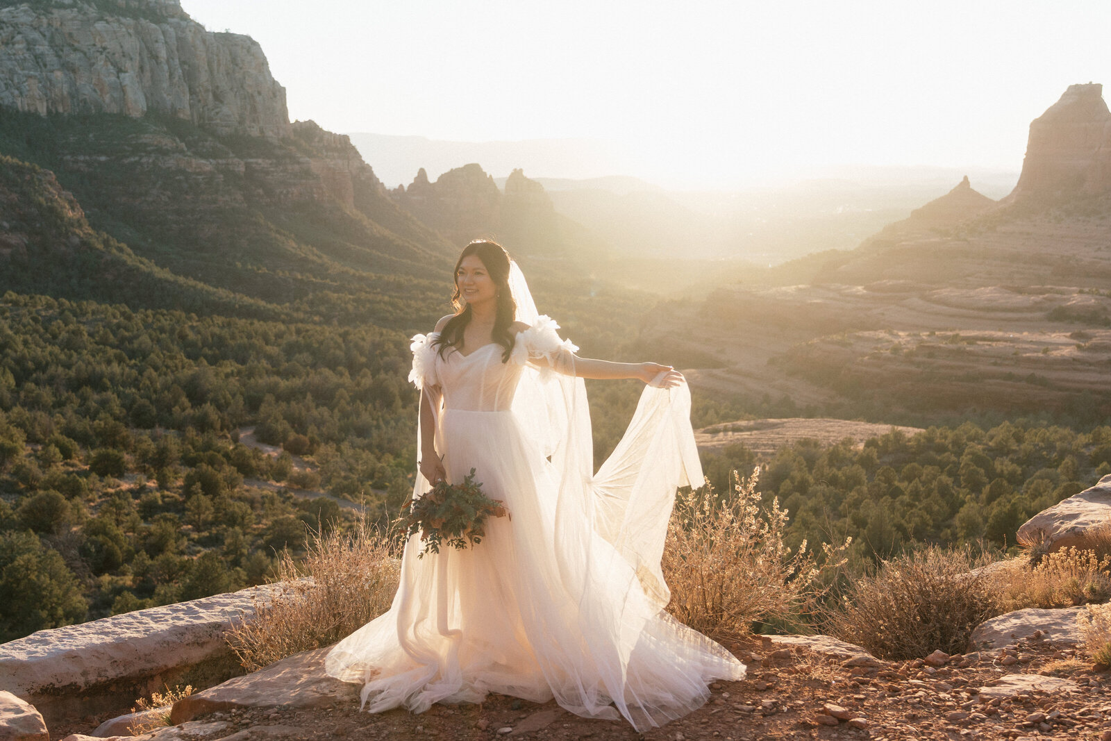 Bride holding her bouquet and veil as she poses on the red rock cliffs of Merry Go Round Rock during golden hour at her Sedona elopement.