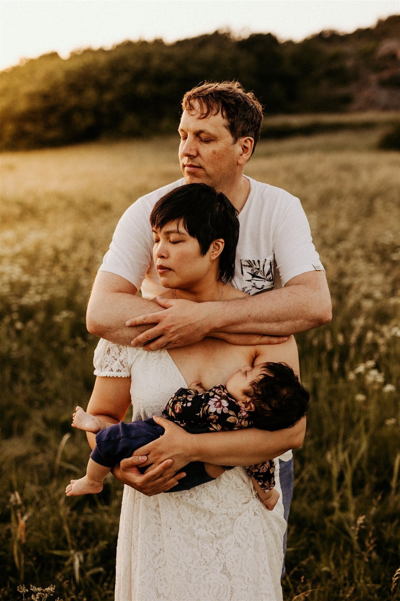 en pappa håller om sin fru och son på ett fält i solnedgången