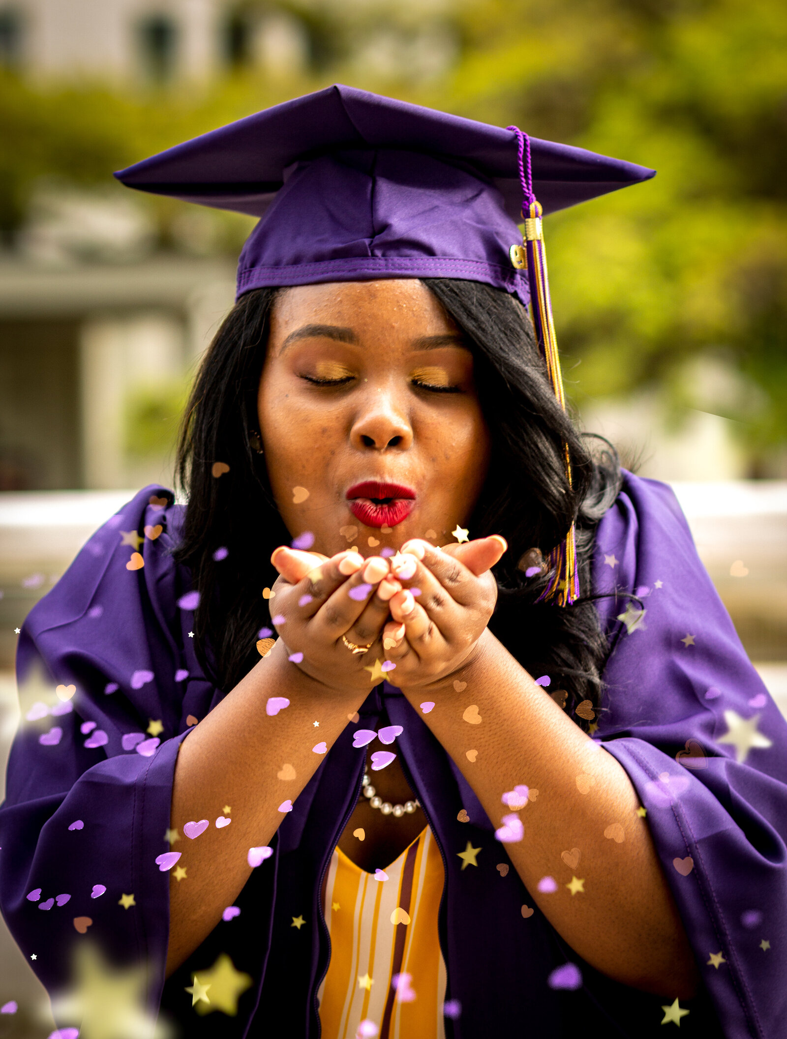 girl in purple graduation cap and gown blowing purple and gold heart glitter