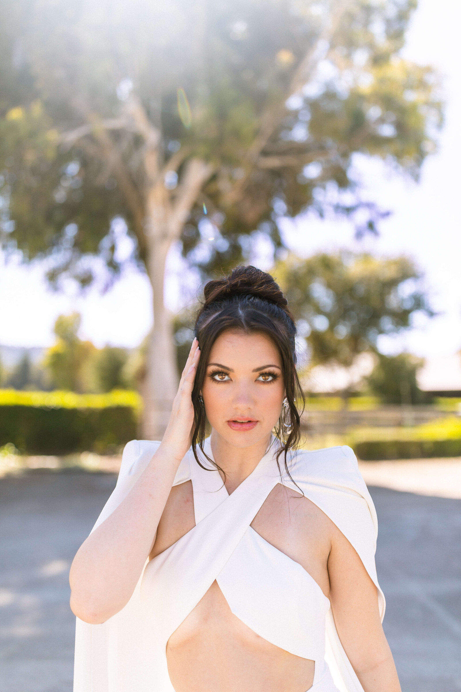 girl with dark hair doing a model pose in an all white outfit in a park